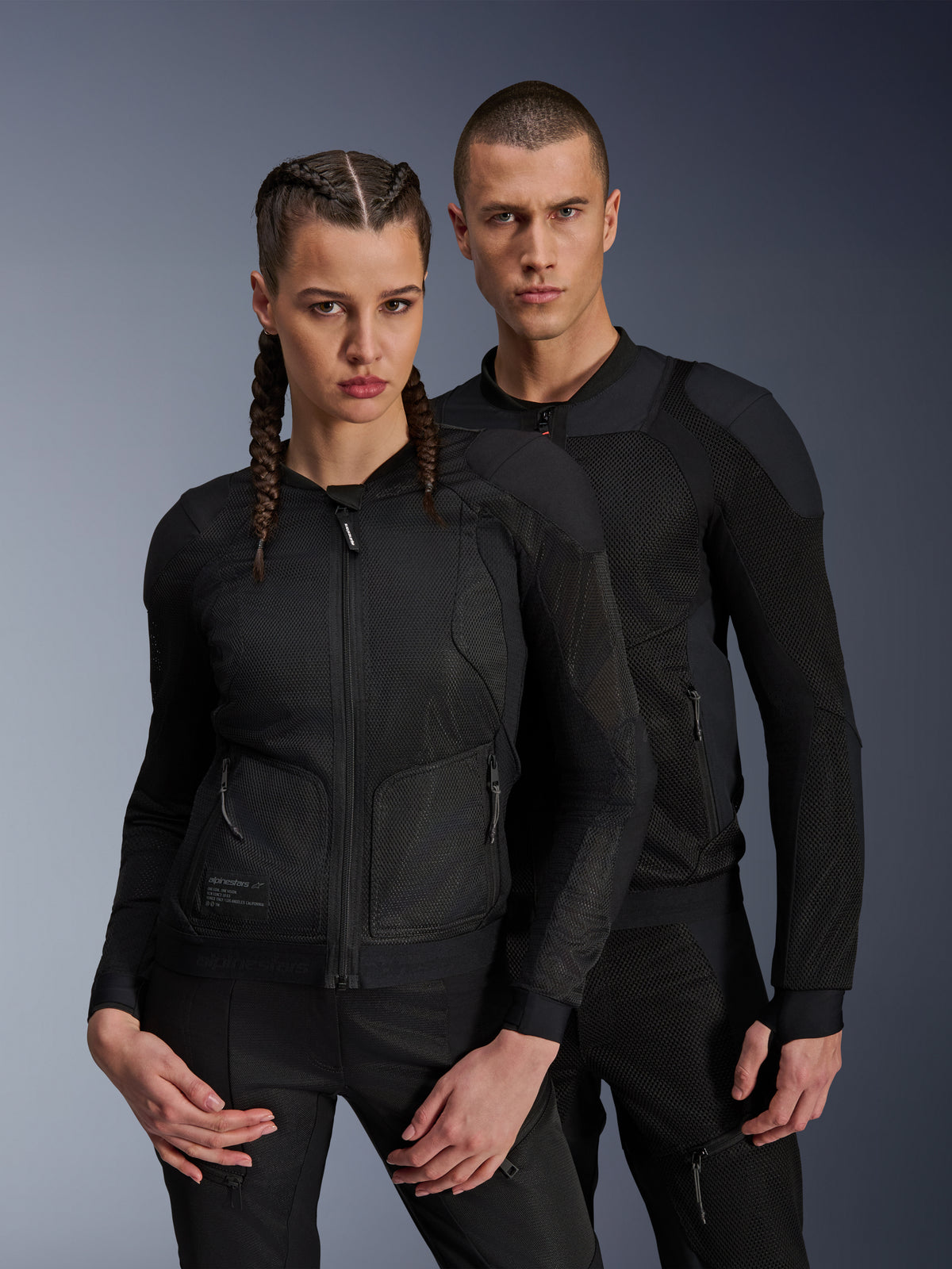Man och kvinna i Alpinestars Troop-Air- och Stella Troop-Air-jackor, svarta tekniska motorcykeljackor i mesh med 2D tech-mesh-struktur för ventilation och förstärkta paneler, modern urban körutrustning.