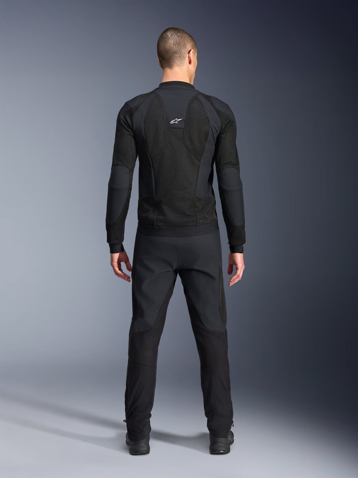 Alpinestars Troop-Air Pro jacka, sedd bakifrån, svart, teknisk motorcykeljacka med stora ventilationspaneler i mesh och vit Alpinestars-logotyp, kombinerad med svarta byxor, urban contemporary-körutrustning