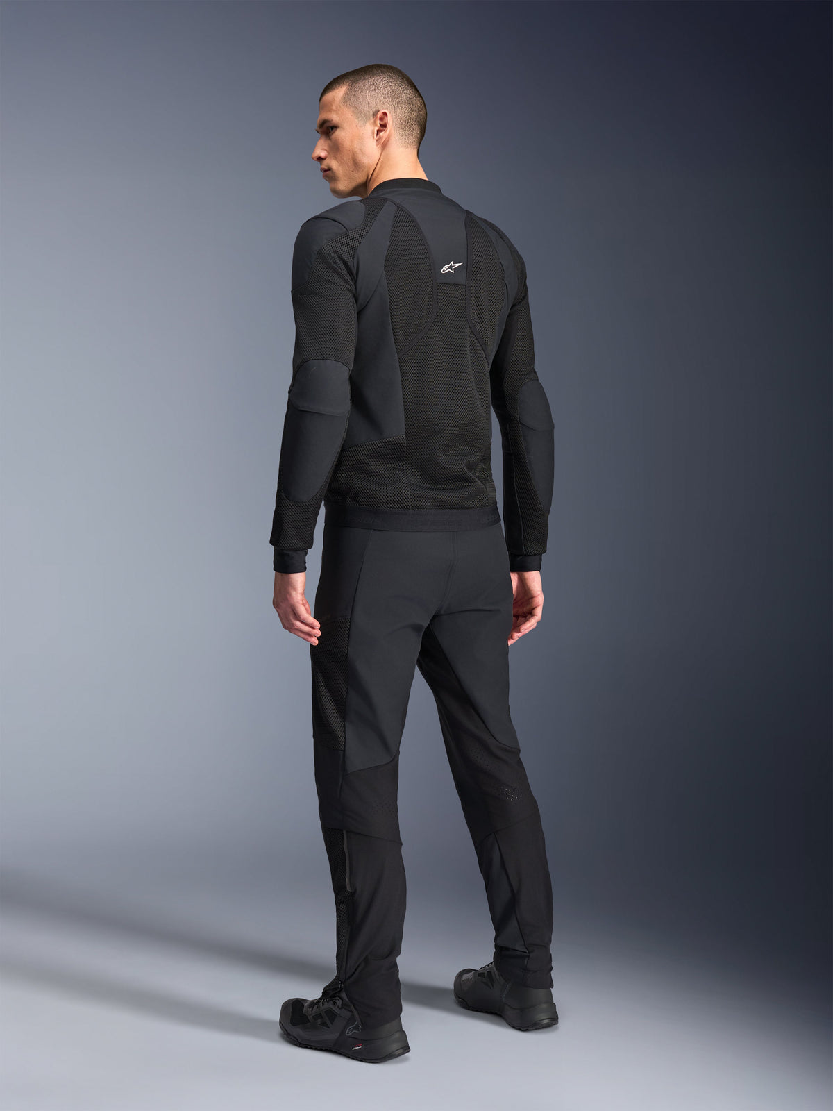 Alpinestars Troop-Air Pro Jacka, svart, teknisk ventilerad skyddsjacka sedd bakifrån, med omfattande meshpaneler för luftflöde, kombinerad med matchande svarta tekniska byxor och skor.