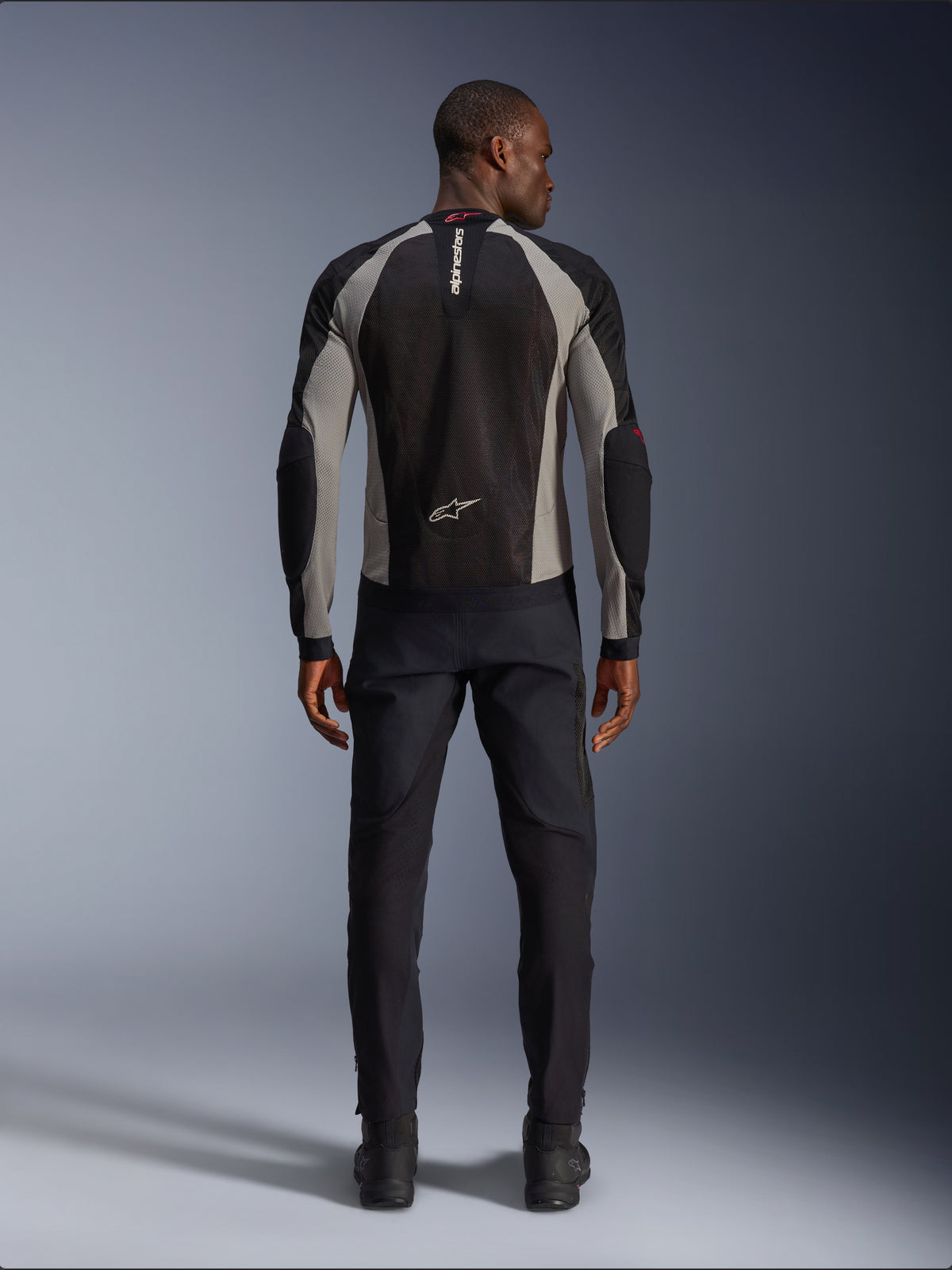 Alpinestars Troop-Air-jacka, motorcykeljacka i Black Ash Gray och Bright Red, sedd bakifrån på manlig modell, lätt mesh-konstruktion för ventilation, Alpinestars-logotyp på kragen och nedre delen av ryggen, matchad med svarta körbyxor