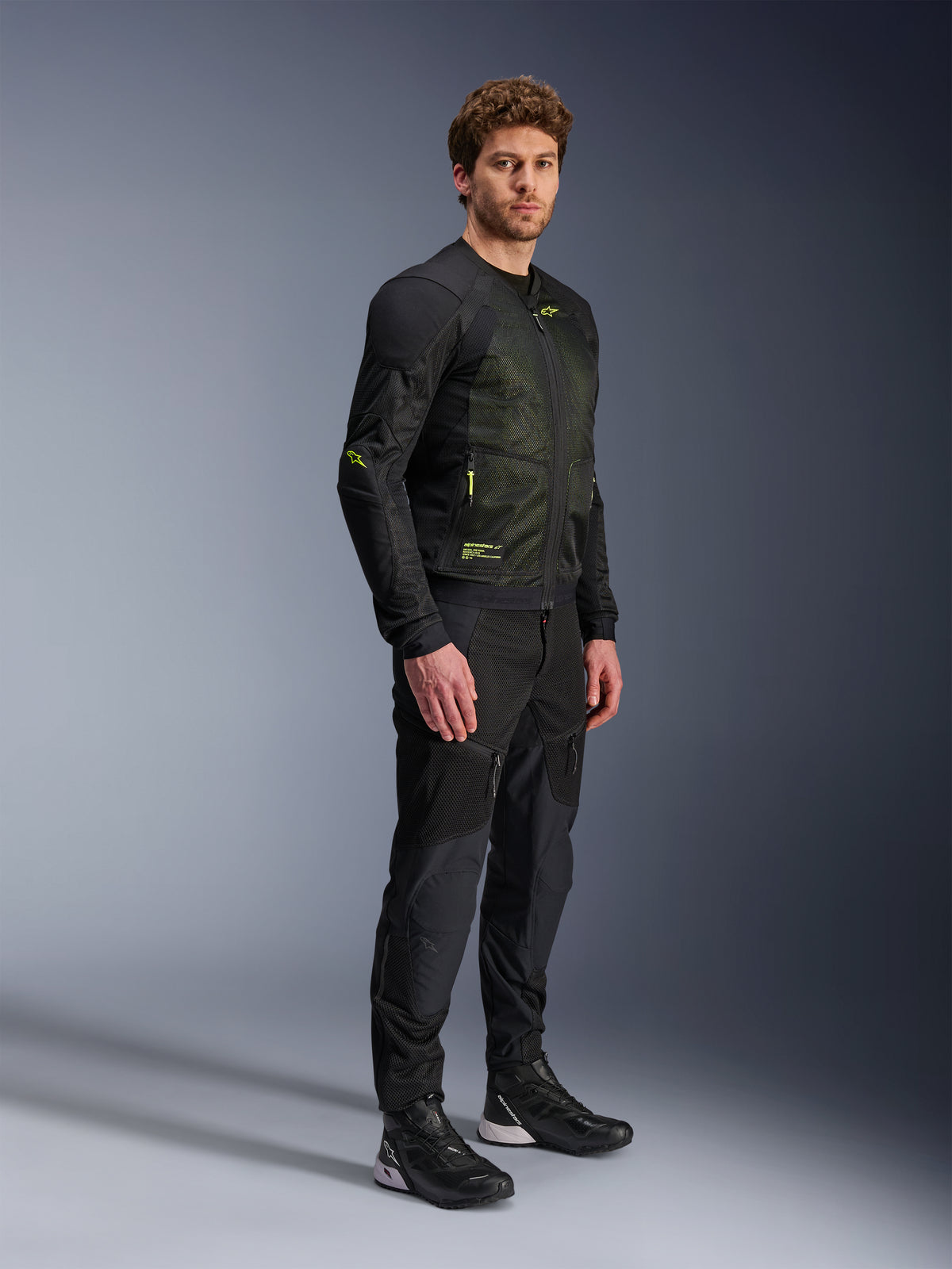 Alpinestars Troop-Air-jacka, motorcykeljacka i mesh, svart och neongul, bärs av en modell med matchande svarta byxor och körskor, har mesh-konstruktion med högt luftflöde och neongula detaljer på bröstet och ärmarna, lätt teknisk design för vägkörning