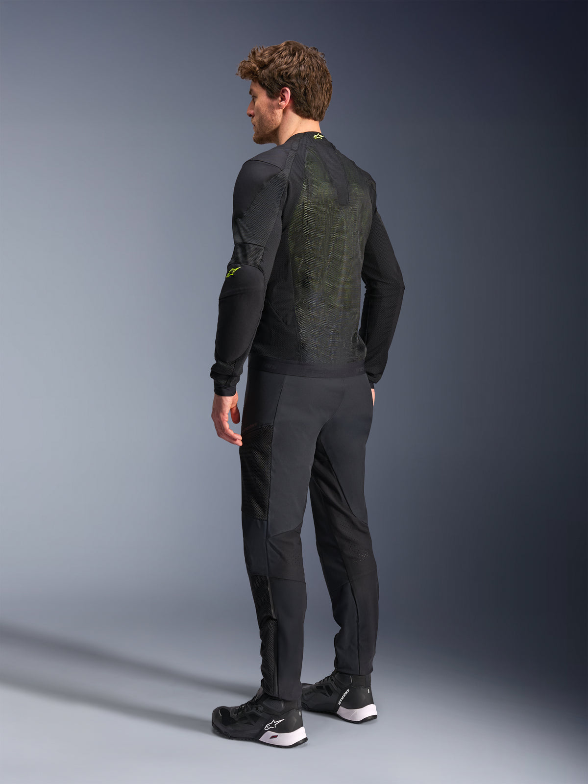 Alpinestars Troop-Air-jacka i svart och neongult, baksida av en manlig modell som bär den tekniska ventilerade jackan, med en stor ryggpanel i mesh med gula detaljer och neongula Alpinestars-logotyper, matchad med svarta motorcykelbyxor.