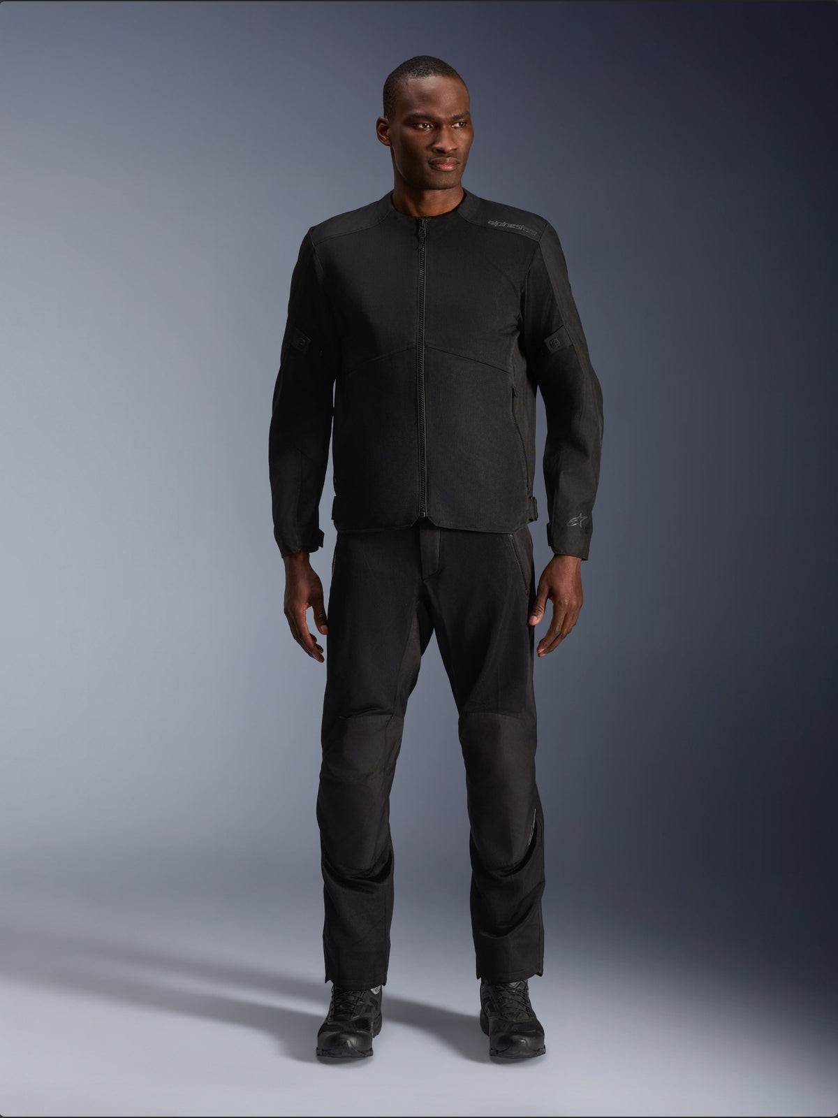 Male model wearing the Alpinestars C-1 Air Jacket in Black, paired with matching black pants and boots, urban motorcycle gear designed for commuting, featuring a clean aesthetic with mesh panels and subtle branding.