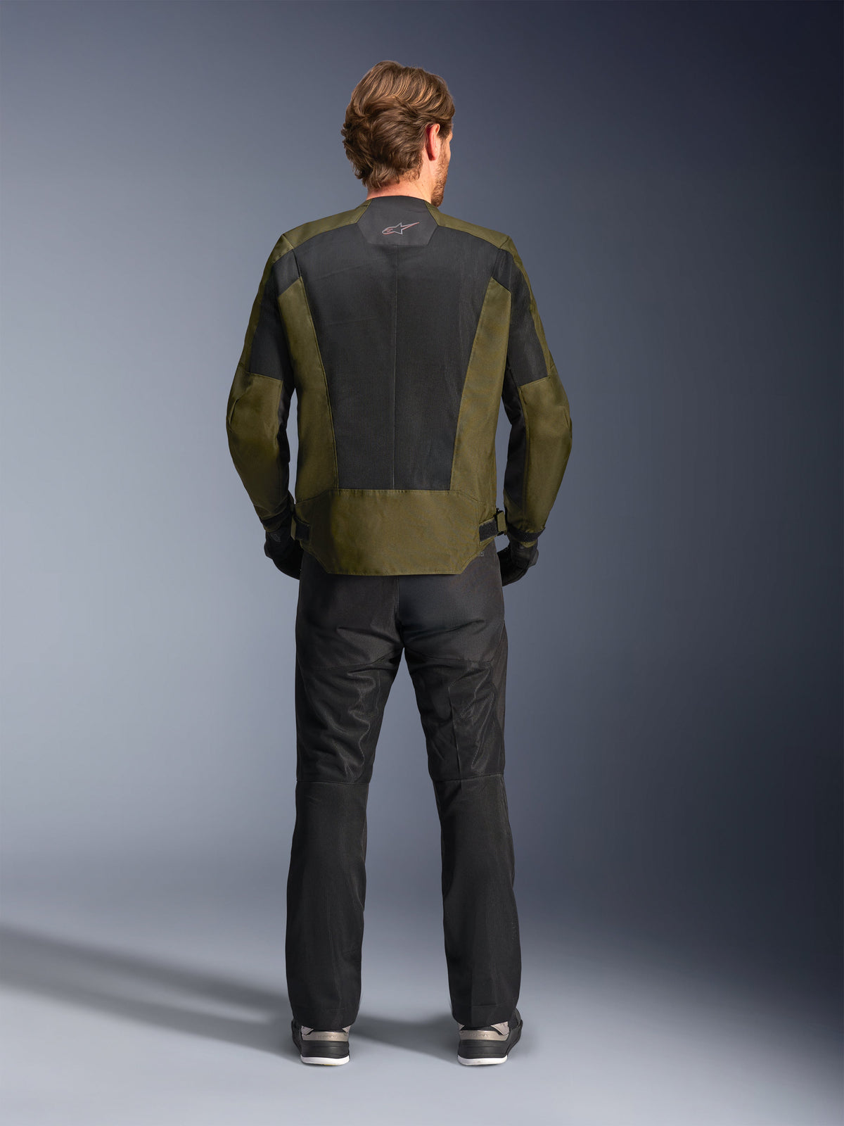 Rear view of a rider wearing the Alpinestars C-1 Air Jacket in Khaki and Black, featuring a large tech mesh back panel for ventilation, paired with black motorcycle pants, urban contemporary road riding gear.