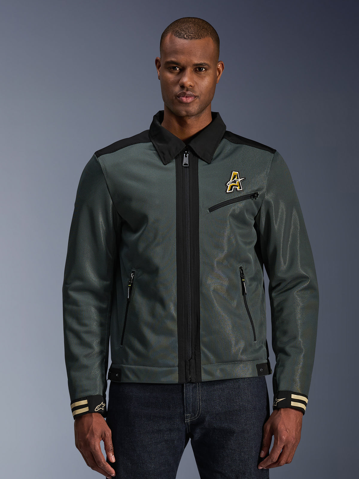 Alpinestars Ignite Air Jacket, urban motorcycle jacket, dark forest green with black accents, featured on model with denim pants, Harrington-style shirt collar, zippered front, chest logo, and striped cuffs, modern mesh and textile construction for summer riding