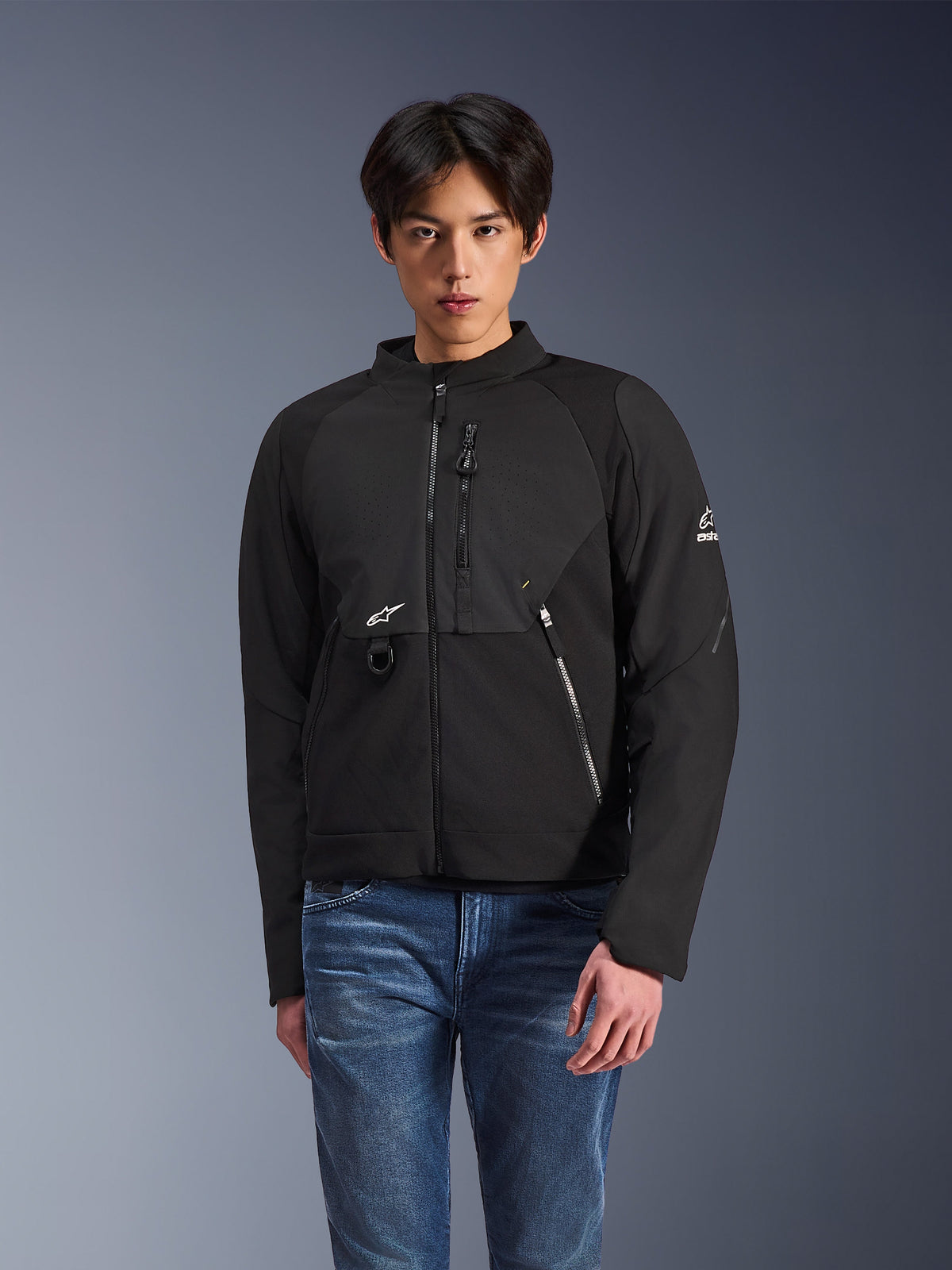 Alpinestars Provoke Jacket, Black Textile Urban Riding Jacket, worn by a male model with blue jeans, featuring laser-perforated chest panels, multiple zippered pockets, white A-star logo on the chest and sleeve, sleek modern design for street riding