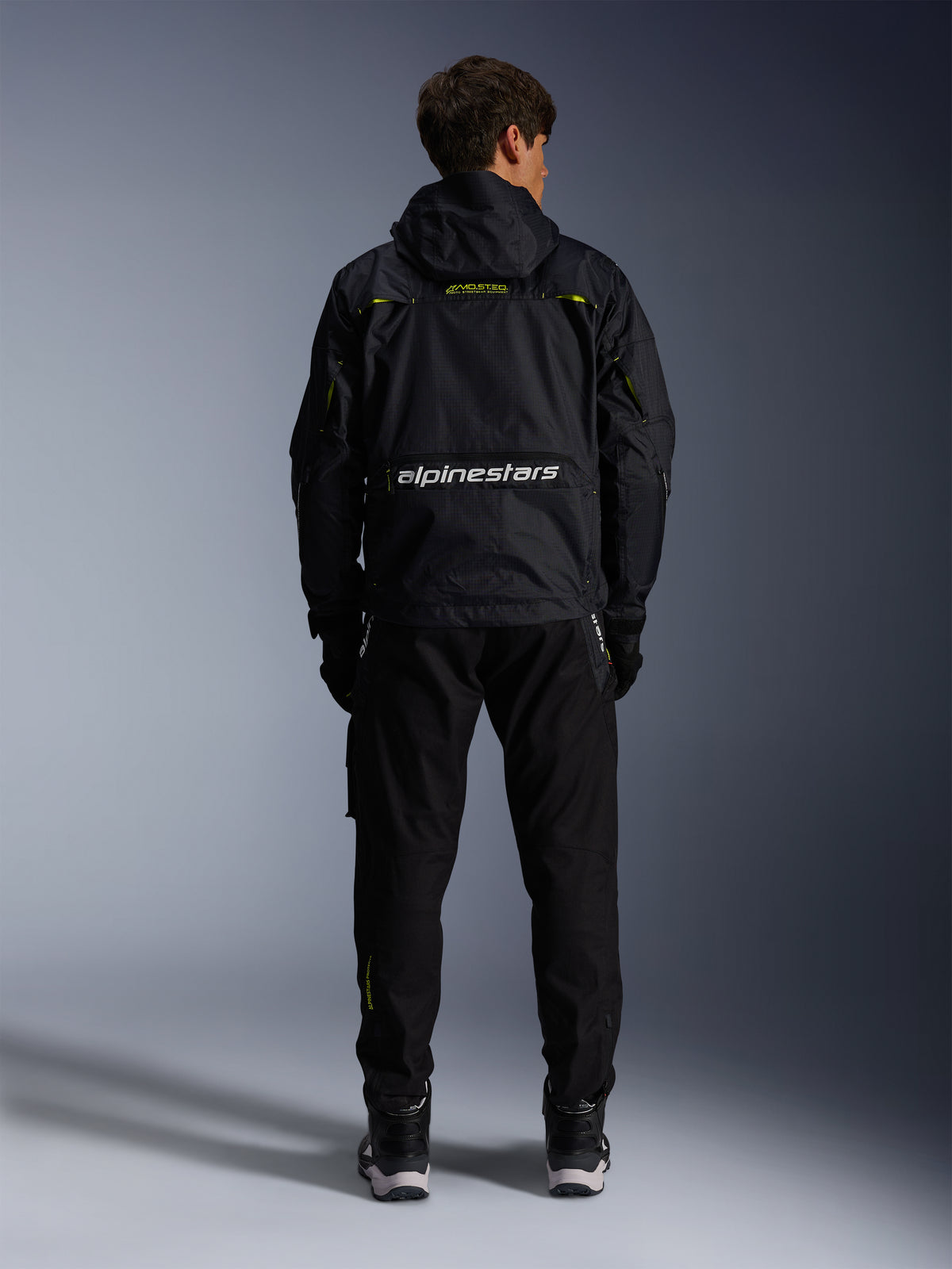 Alpinestars Mogress Air jacka, urban motorcykeljacka i svart och lime punch textil, vy bakifrån med vit logotyp, bärs av modell med svarta byxor och stövlar.