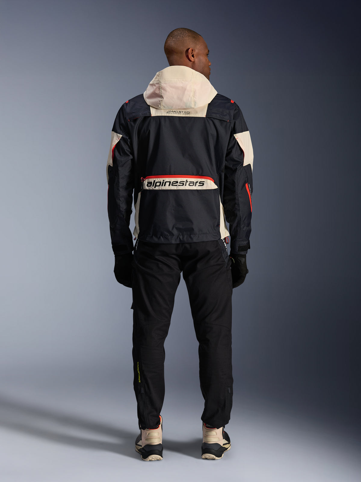 Alpinestars Mogress Air jacka, urban motorcykeljacka för herr, vy bakifrån i svart och orange med huva, ripstop-tyg och logotyp.