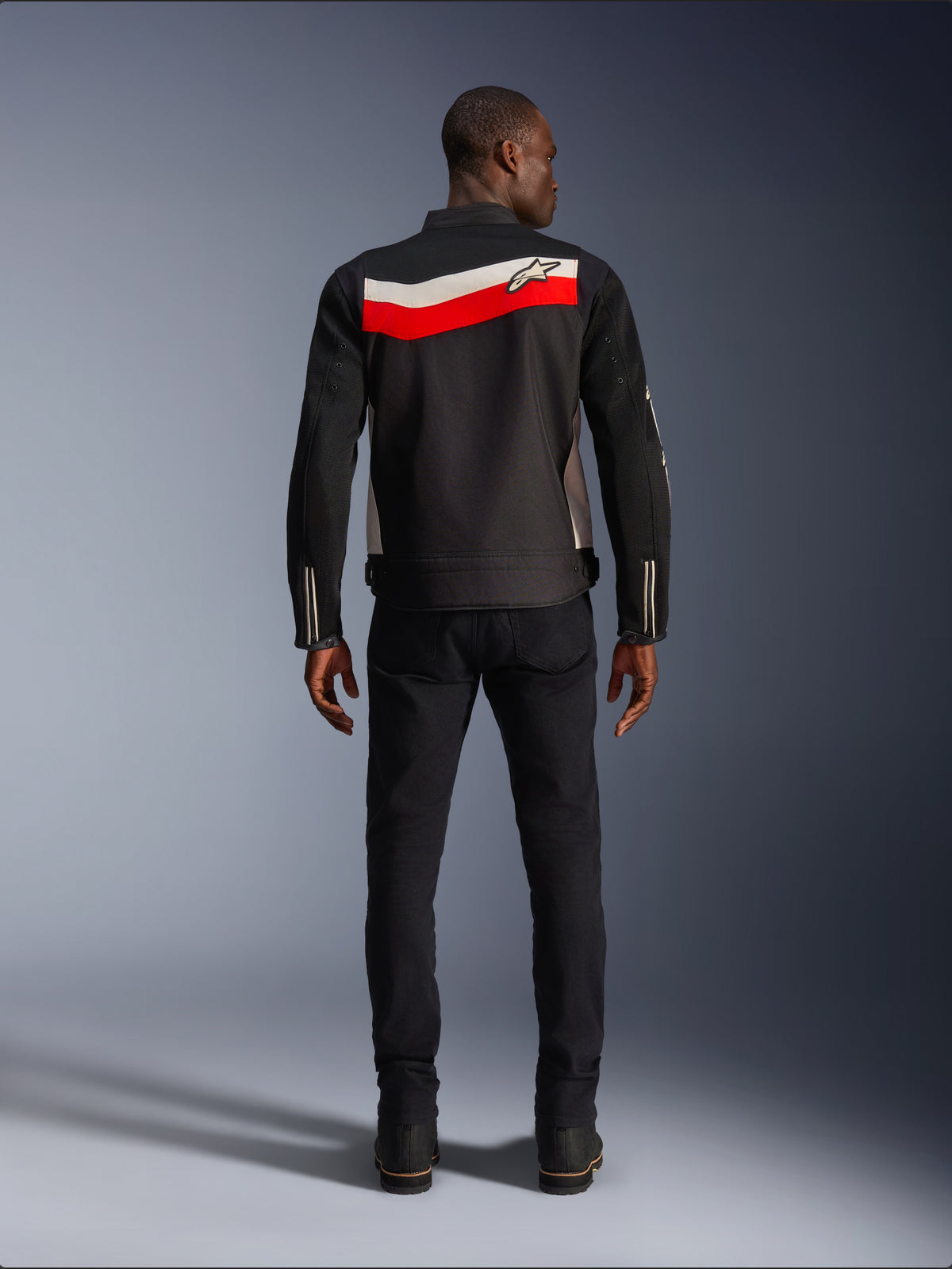 Alpinestars T-Dyno Air Jacka, motorcykeljacka i textil för herrar, vy bakifrån, svart med klarröda och ecru-färgade horisontella ränder över ryggen, Alpinestars-logotyp på oket, bärs med svarta byxor och stövlar, ventilerande 3D-mesh-konstruktion