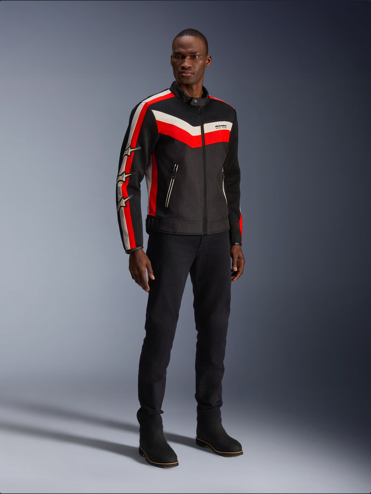 Alpinestars T-Dyno Air-jacka, Black Bright Red Ecru, mc-textiljacka för herrar med 3D-meshpaneler, röda och vita chevron-ränder på bröstet och stjärnlogotyper på ärmarna, bärs av en modell med svarta byxor och stövlar.