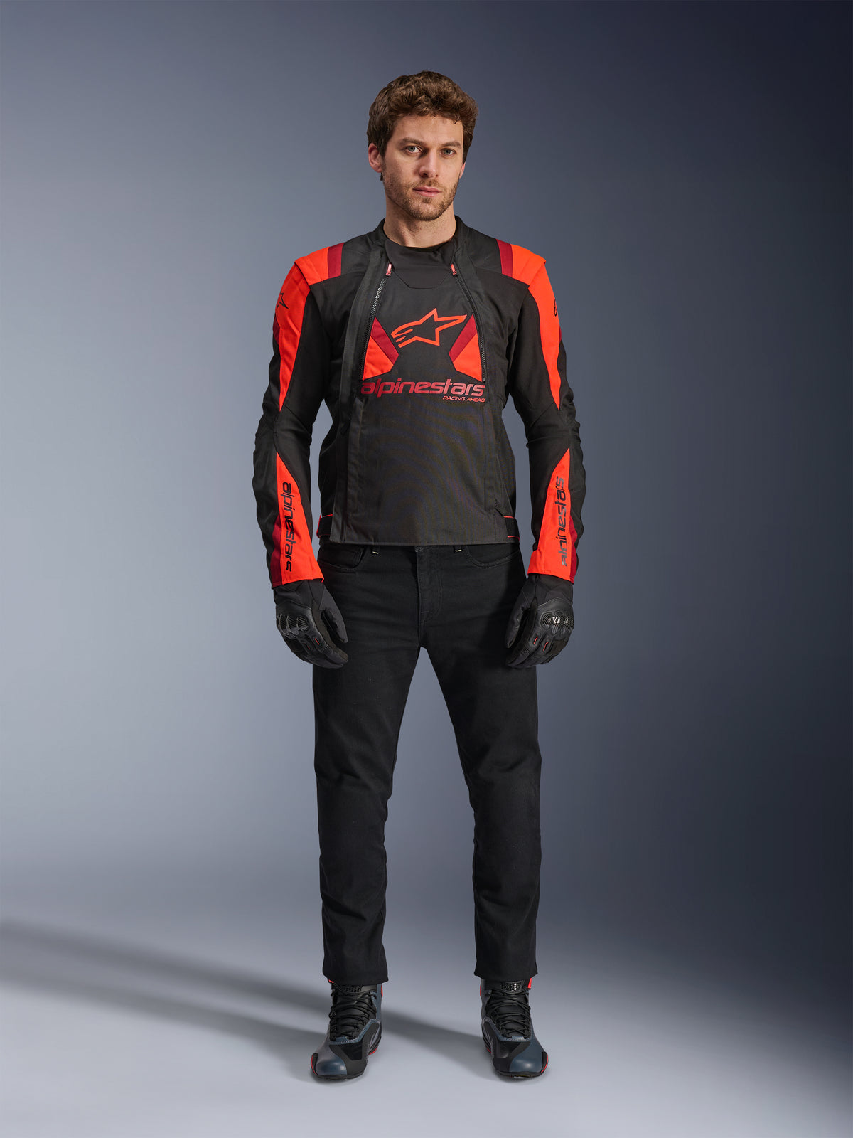 Alpinestars T-Stunt Air Jacket, Black Red Fluo and Dark Red, worn by a model with black riding jeans and gloves, featuring a modular 2-in-1 design with prominent mesh panels for airflow, sport-cut motorcycle gear for road riding