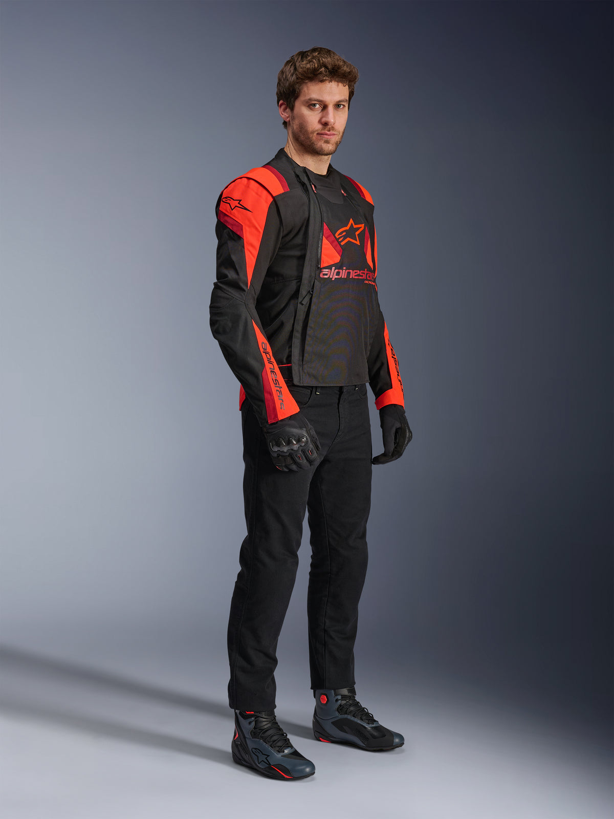 Alpinestars T-Stunt Air Jacket, Black, Red Fluo, and Dark Red, modular motorcycle jacket worn by a model with front panels open to reveal the mesh interior, paired with black riding pants, gloves, and shoes.