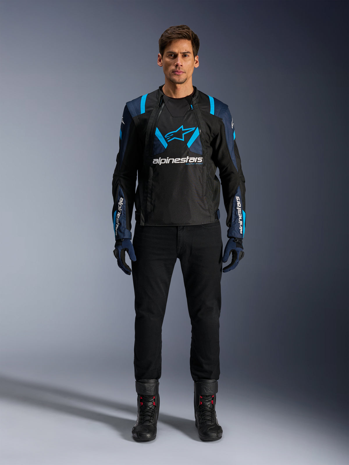 Alpinestars T-Stunt Air Jacket, Motorcycle Jacket, Black with Dark Blue and Bright Blue accents, featuring a large white logo on the chest, sport-cut mesh construction for airflow, worn with black riding pants and boots for a sleek road riding aesthetic.