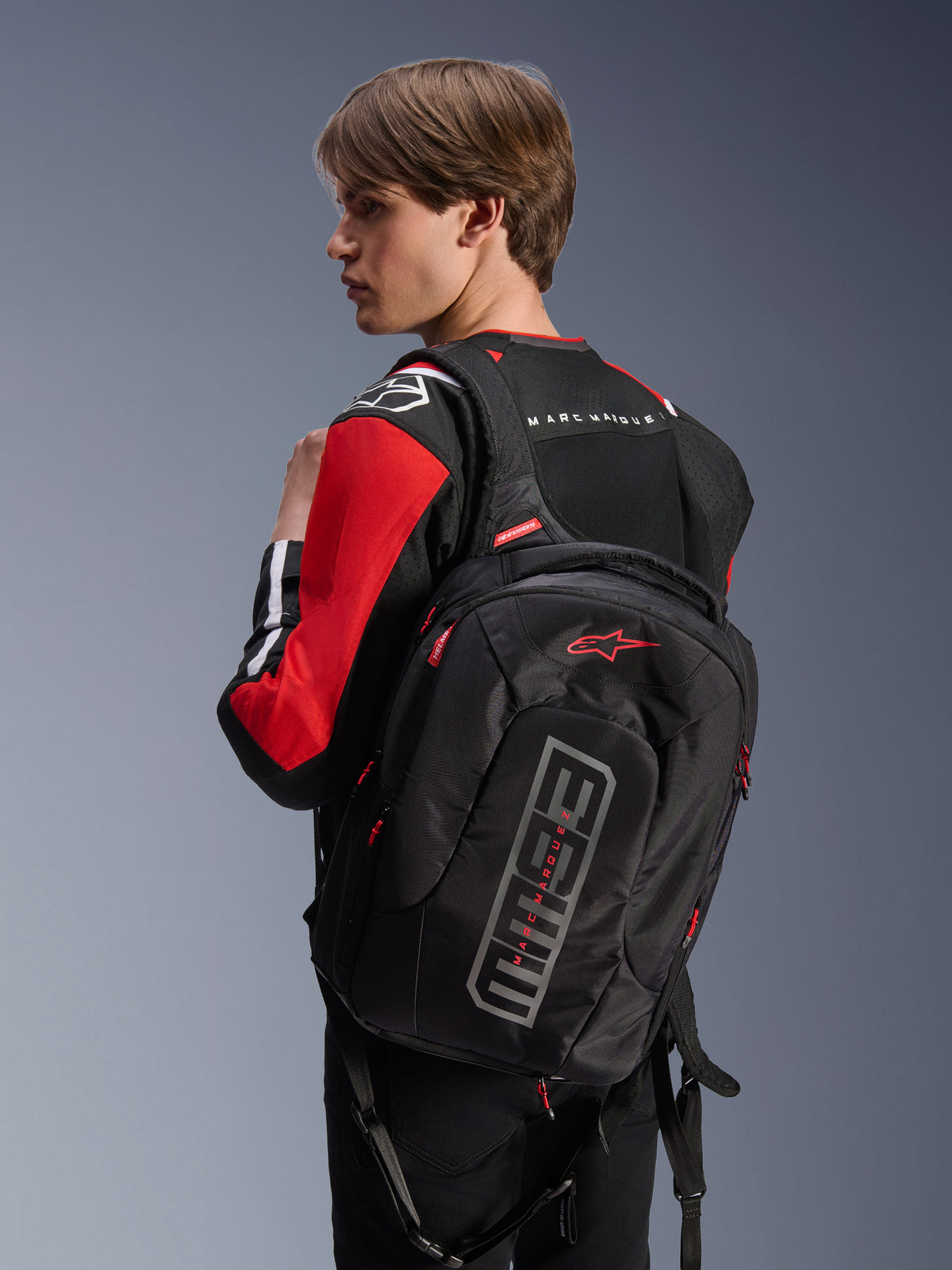 Alpinestars MM93 City Hunter V2 ryggsäck, svart, med röd Astars-logotyp och grå MM93-grafik, bärs av en förare i en röd och svart motorcykeljacka, urban körutrustning från Marc Márquez-kollektionen