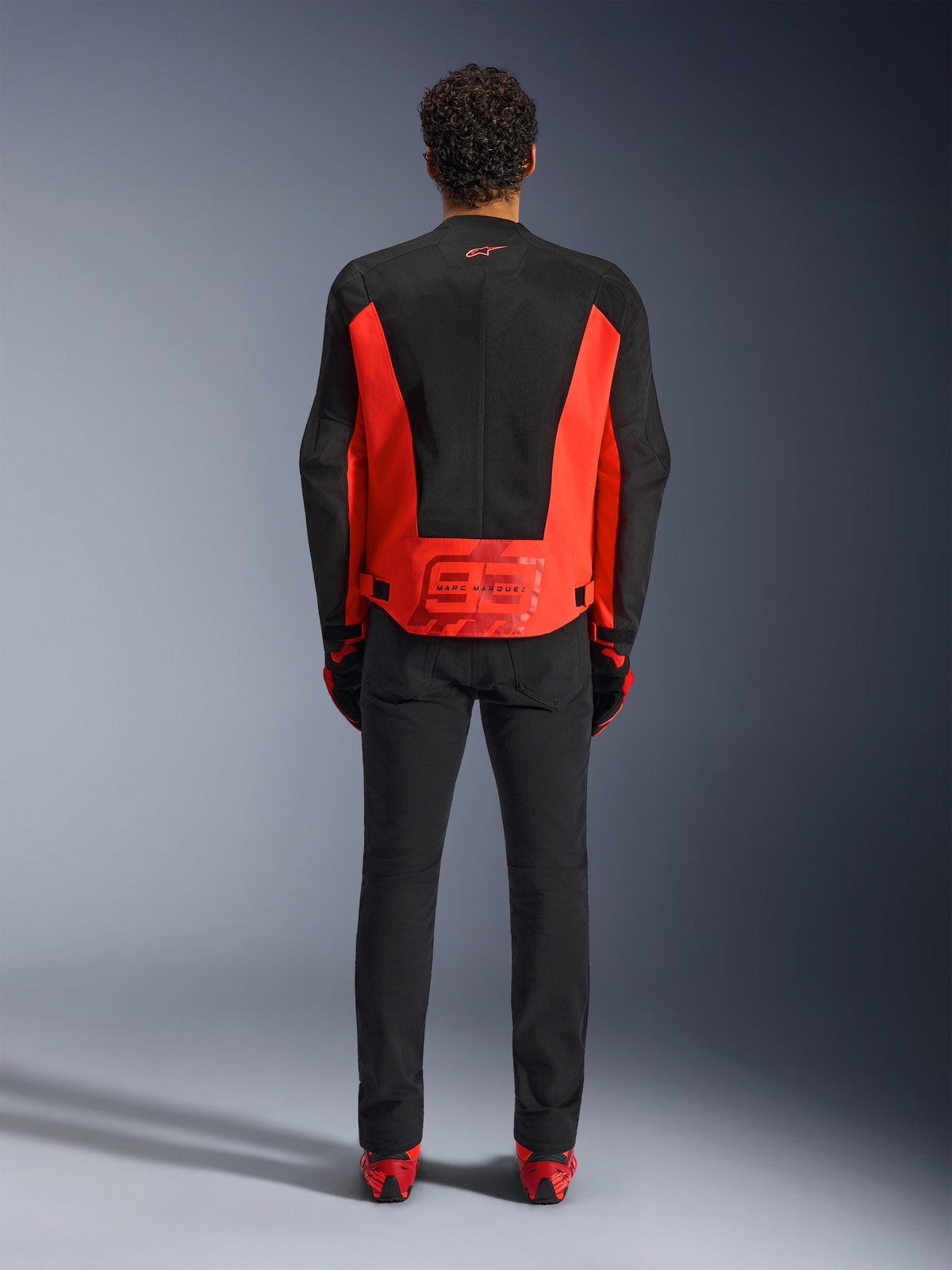Alpinestars MM93 C-1 Air Jacket, Motorcycle Riding Jacket, Red Fluo and Black, rear view featuring the Marc Marquez 93 graphic on the lower back, tech mesh panels for ventilation, paired with black pants and red-accented gear