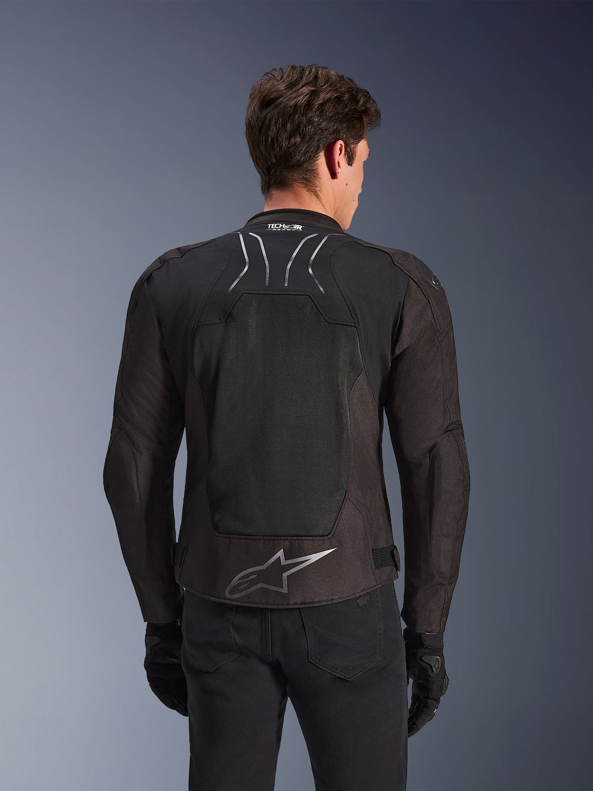 Alpinestars SMX Air-jacka i Black Anthracite, sedd bakifrån på en modell, med en stor tech mesh-ryggpanel för ventilation, Tech-Air Ready-märkning på kragen och en silverfärgad Astar-logotyp på nedre delen av ryggen, kombinerad med svarta handskar och mc-byxor.