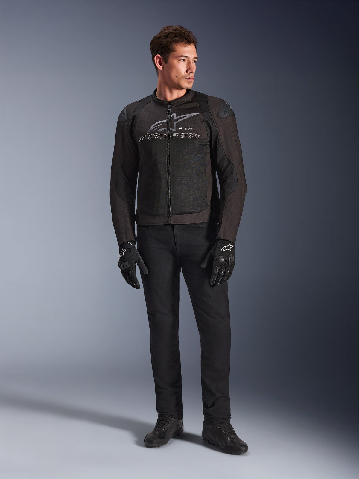 Manlig modell som bär Alpinestars SMX Air Jacket, motorcykeljacka i färgen Black Anthracite med ventilerade meshpaneler och grå logotyp på bröstet, matchad med svarta byxor och skyddshandskar, studiomiljö med tonad bakgrund