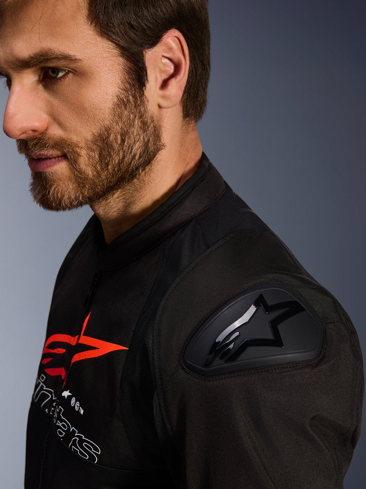 Alpinestars SMX Air-jacka, svart och röd, närbild på DFS Lite-axelskydd med stjärnlogotyp, bärs av en man med skägg, racing- och sportmotorcykeljacka i textil.