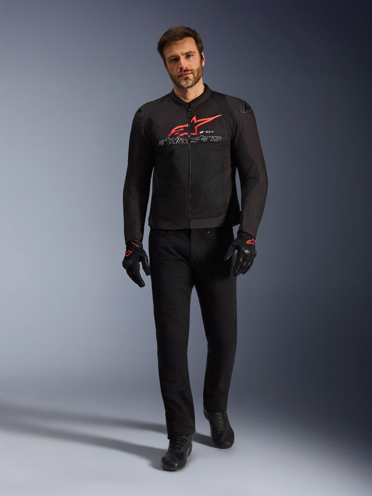 Alpinestars SMX Air Jacka, svart, klar röd och vit, sportig motorcykeljacka buren med svarta körbyxor och handskar, med tekniska meshpaneler och en framträdande röd Alpinestars-logotyp på bröstet, outfit för högpresterande gatkörning