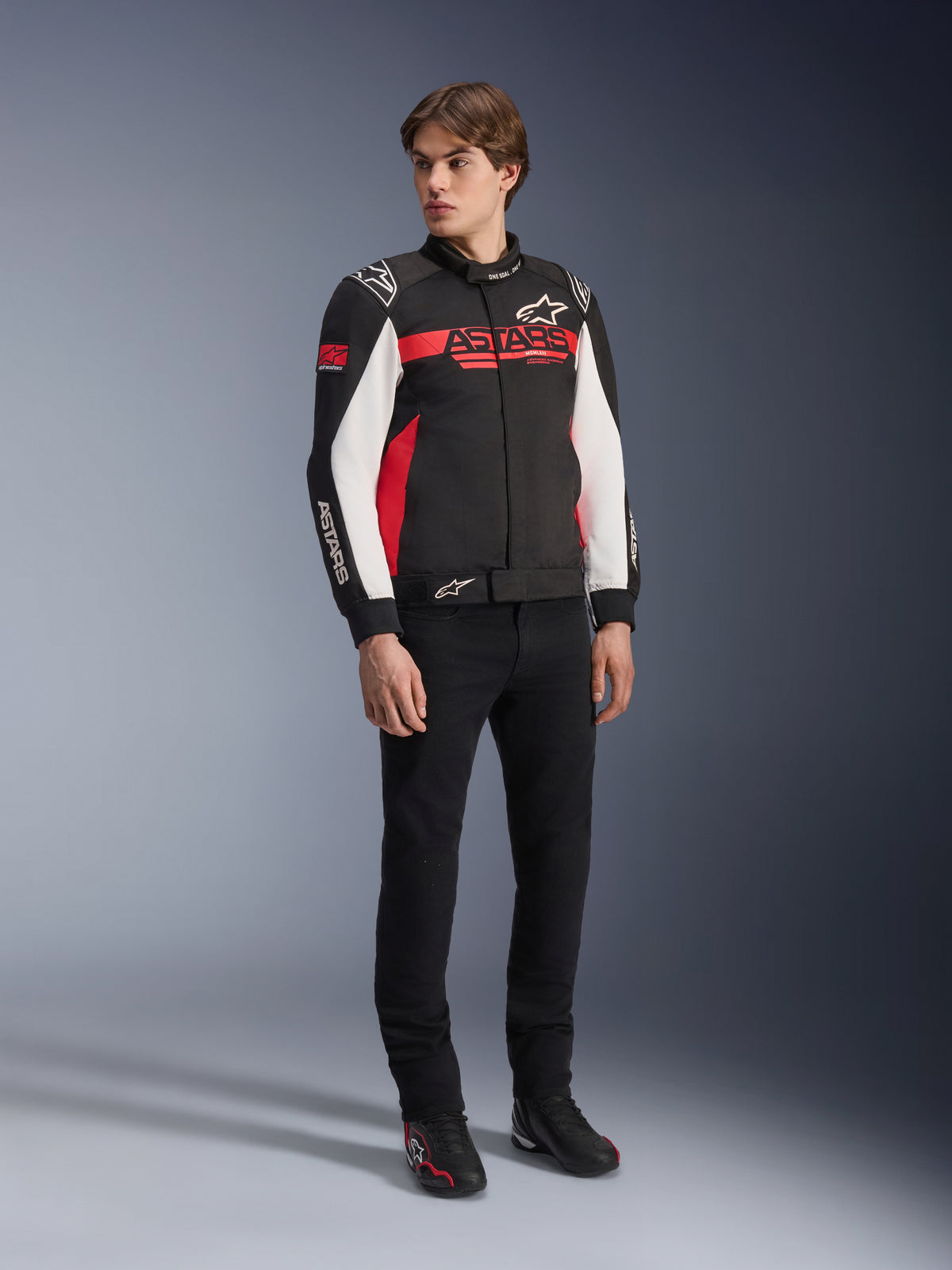 Alpinestars Monza Sport-jacka, svart, klarröd och vit, motorcykeljacka i textil, racinginspirerad design med ASTARS-logotyper på bröstet och ärmarna, bärs av en modell med svarta byxor och körskor, avslappnad sportig körutrustning
