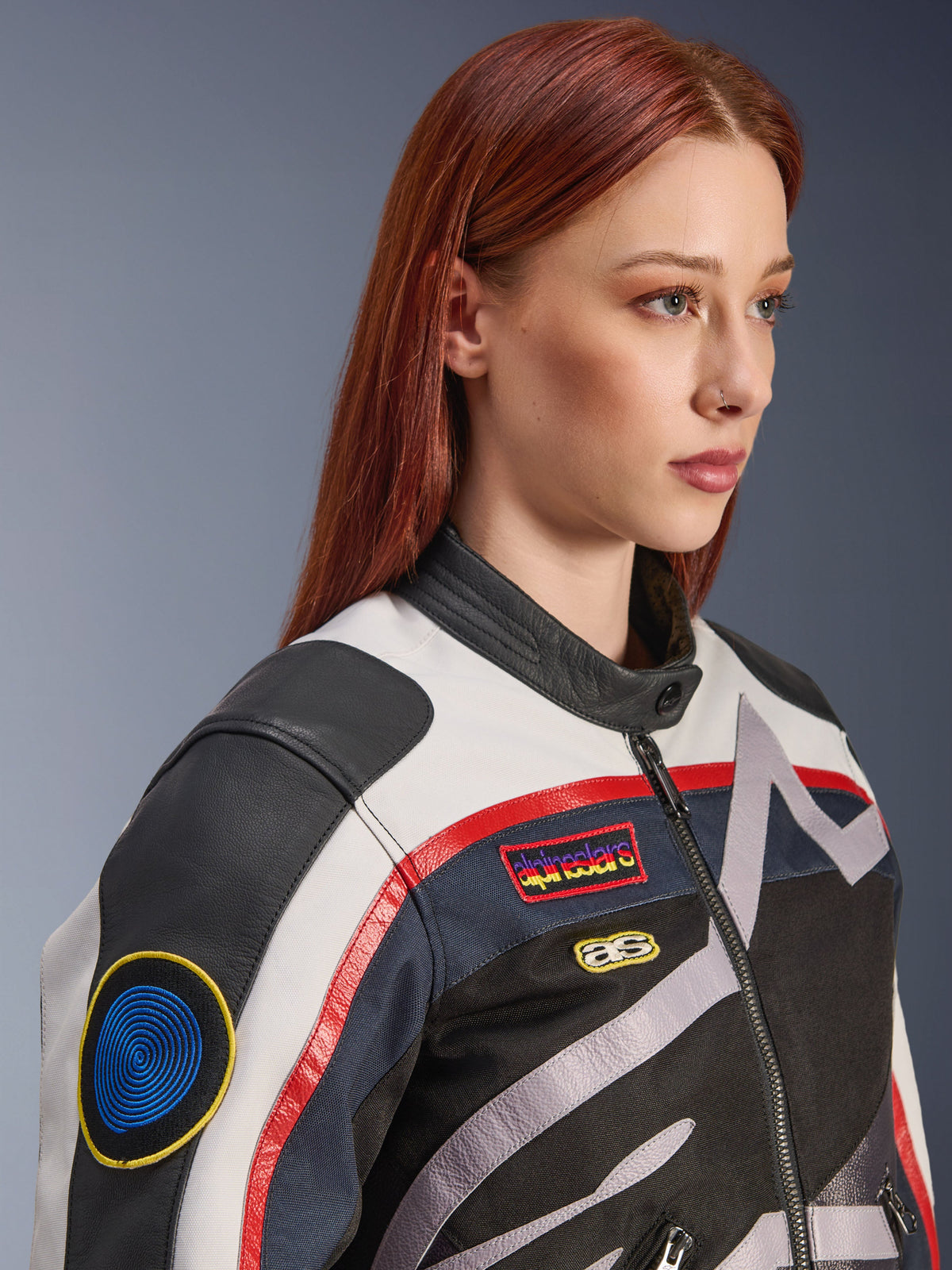 Alpinestars Idles damjacka, off-white, röd och svart, med vintageinspirerade racingmärken och en omslutande logotyp, textil- och läderkonstruktion, urban motorcykelstil buren av en modell.