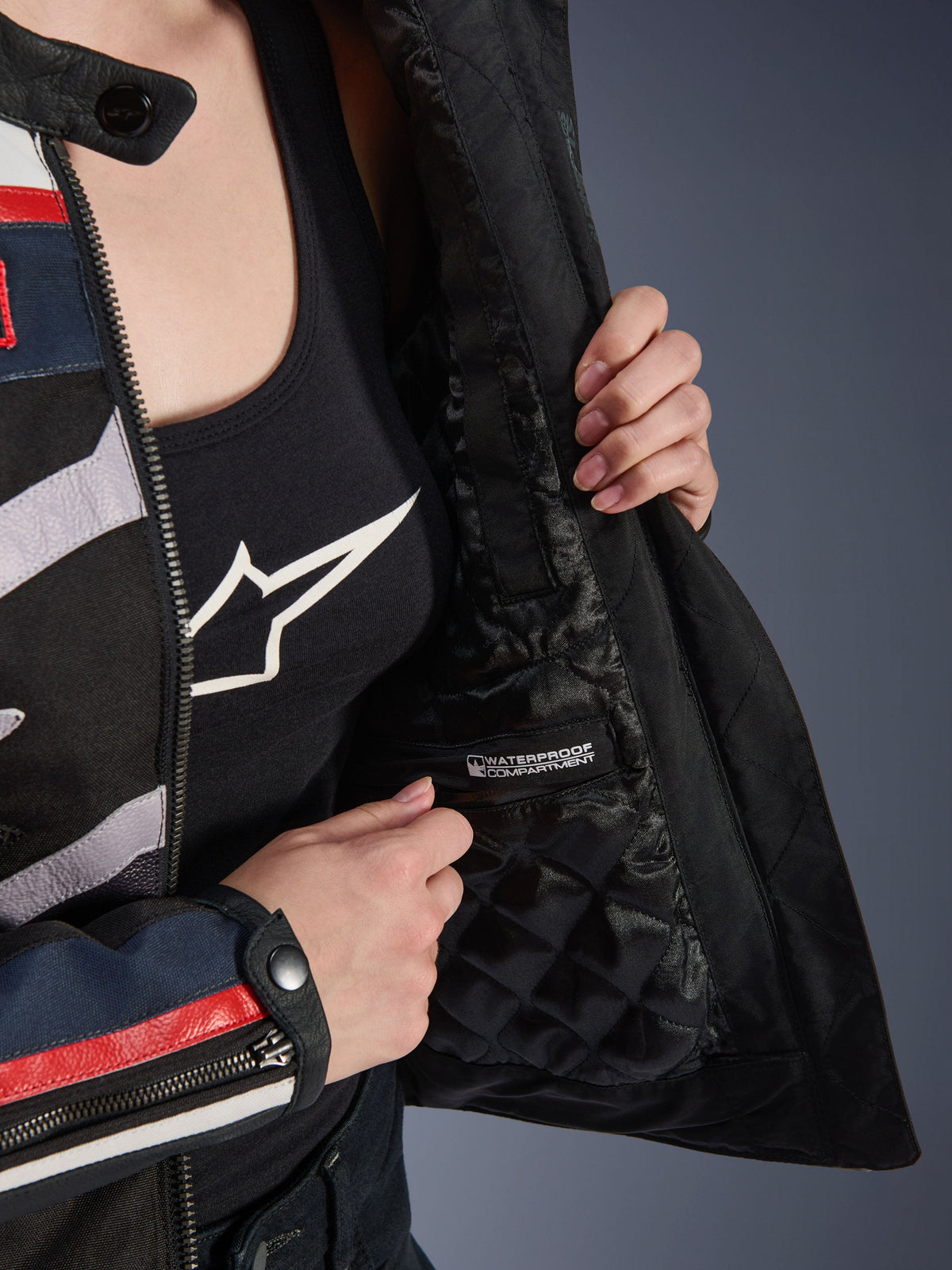 Alpinestars Idles damjacka, interiördetalj som visar svart kviltat foder och märkt vattentätt fack, bärs över ett svart linne med logotyp, funktionell motorcykelutrustning för damer