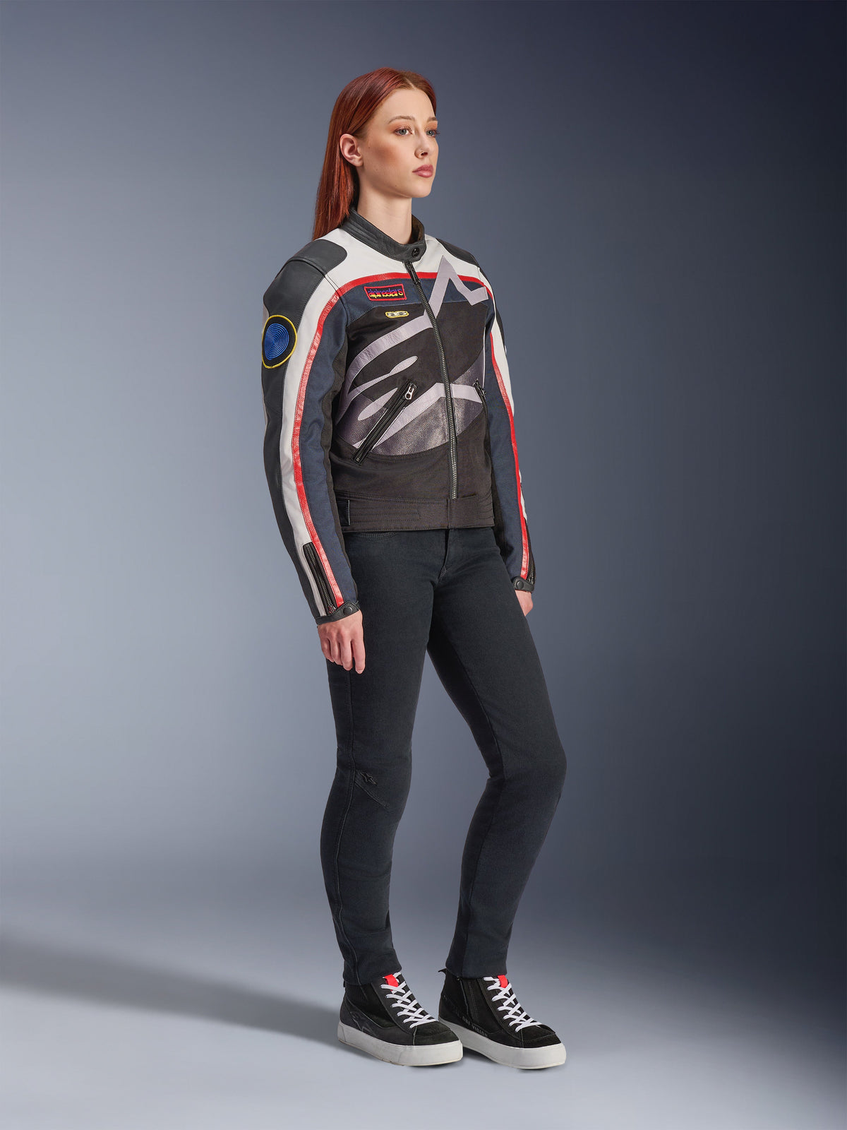 Alpinestars Idles damjacka, motorcykeljacka, benvit, röd och svart, med en stor omslutande Alpinestars-logotyp och vintage racing-inspirerade märken, bärs med svarta byxor och höga sneakers, modern urban mc-utrustning