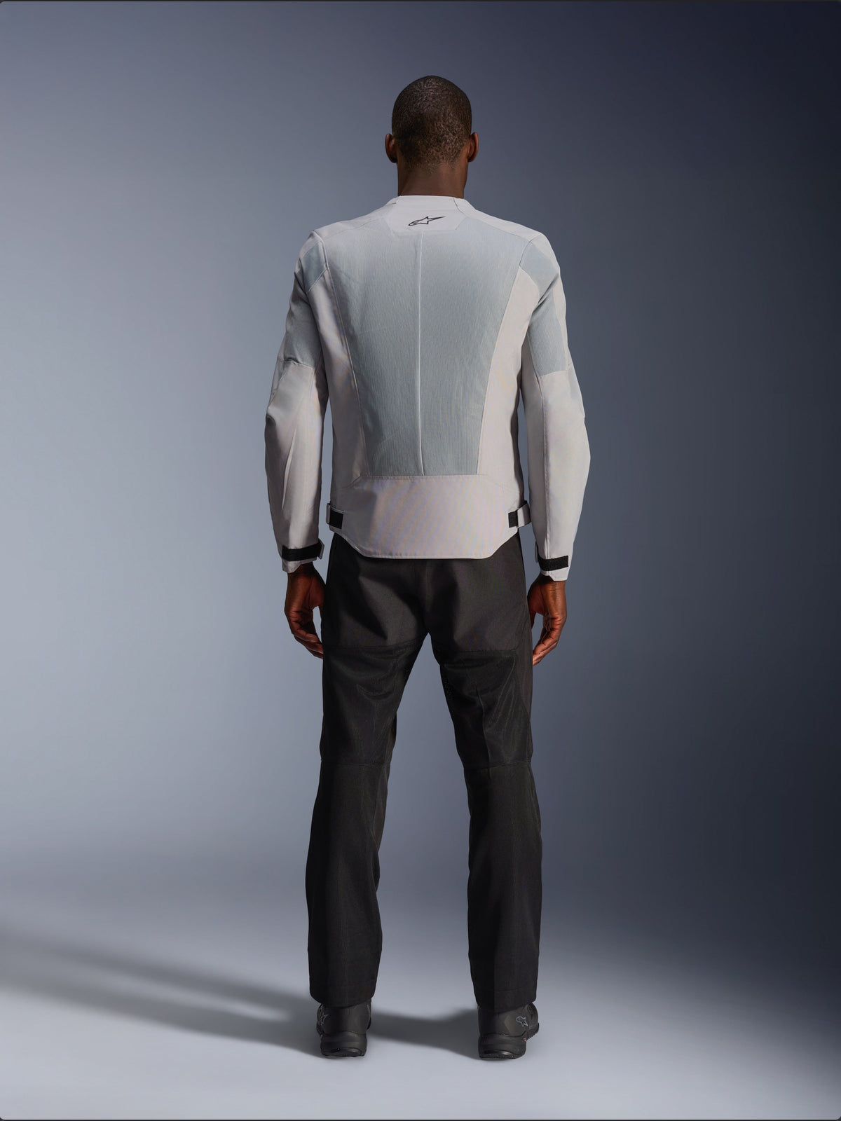 Alpinestars C-1 Air-jacka i silver, sedd bakifrån på en manlig modell, MC-jacka i textil med stora ventilationspaneler i teknisk mesh, liten svart logotyp i nacken och midjejusteringar, bärs med svarta körbyxor för en modern urban look.