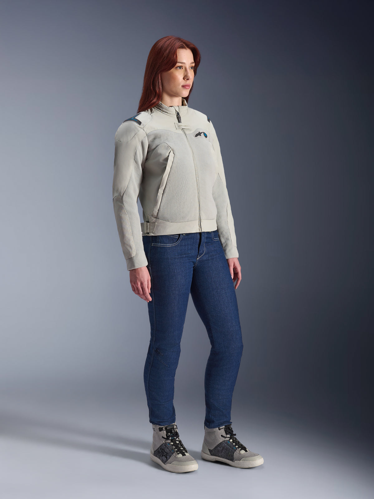 Kvinna som bär Alpinestars Stella Circal-1 Air Jacket i Metal Gray och Methyl Blue, kombinerat med blå jeans och urbana mc-skor, vilket framhäver jackans meshpaneler och minimalistiska urbana design.