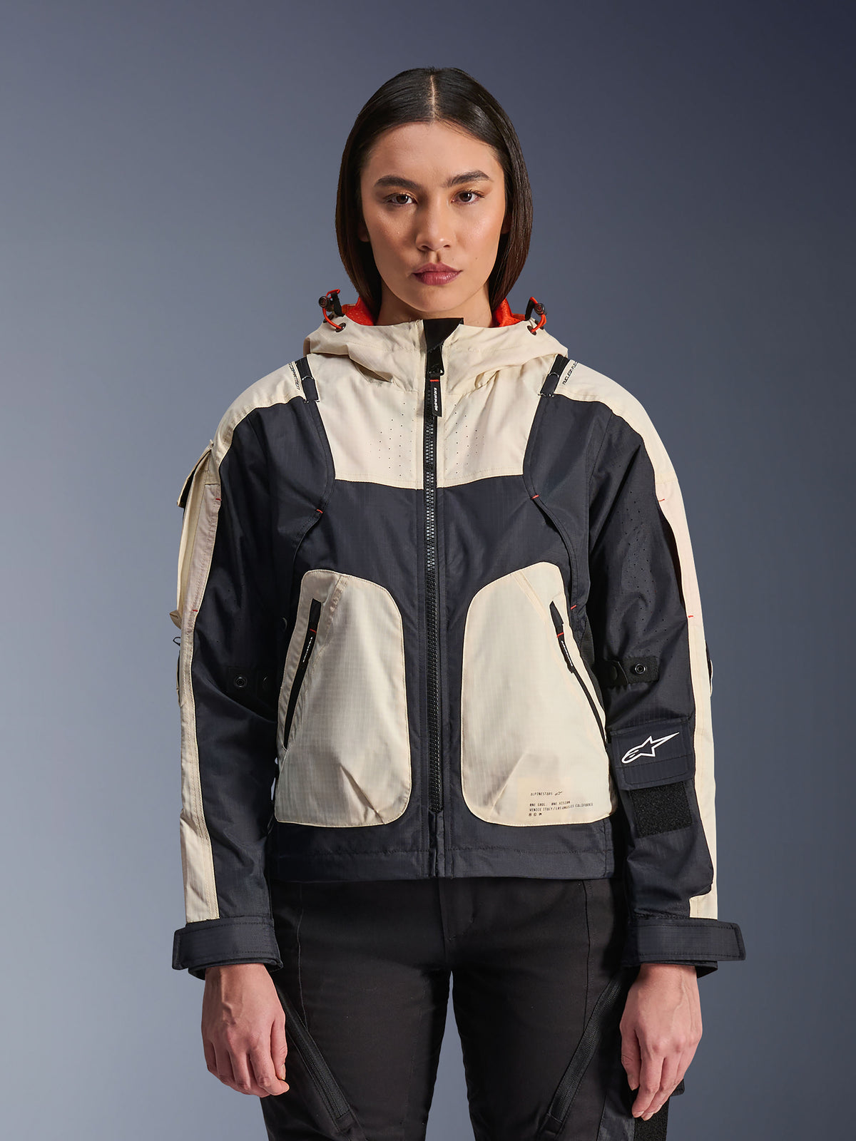 Alpinestars Molly Air Jacket, urban motorcykeljacka för dam, Black Almond, frontvy på en modell, krämvita och svarta ripstop-paneler, huva med orange foder, dragkedja framtill och stora utility-fickor, modern streetwear-inspirerad motorcykelutrustning