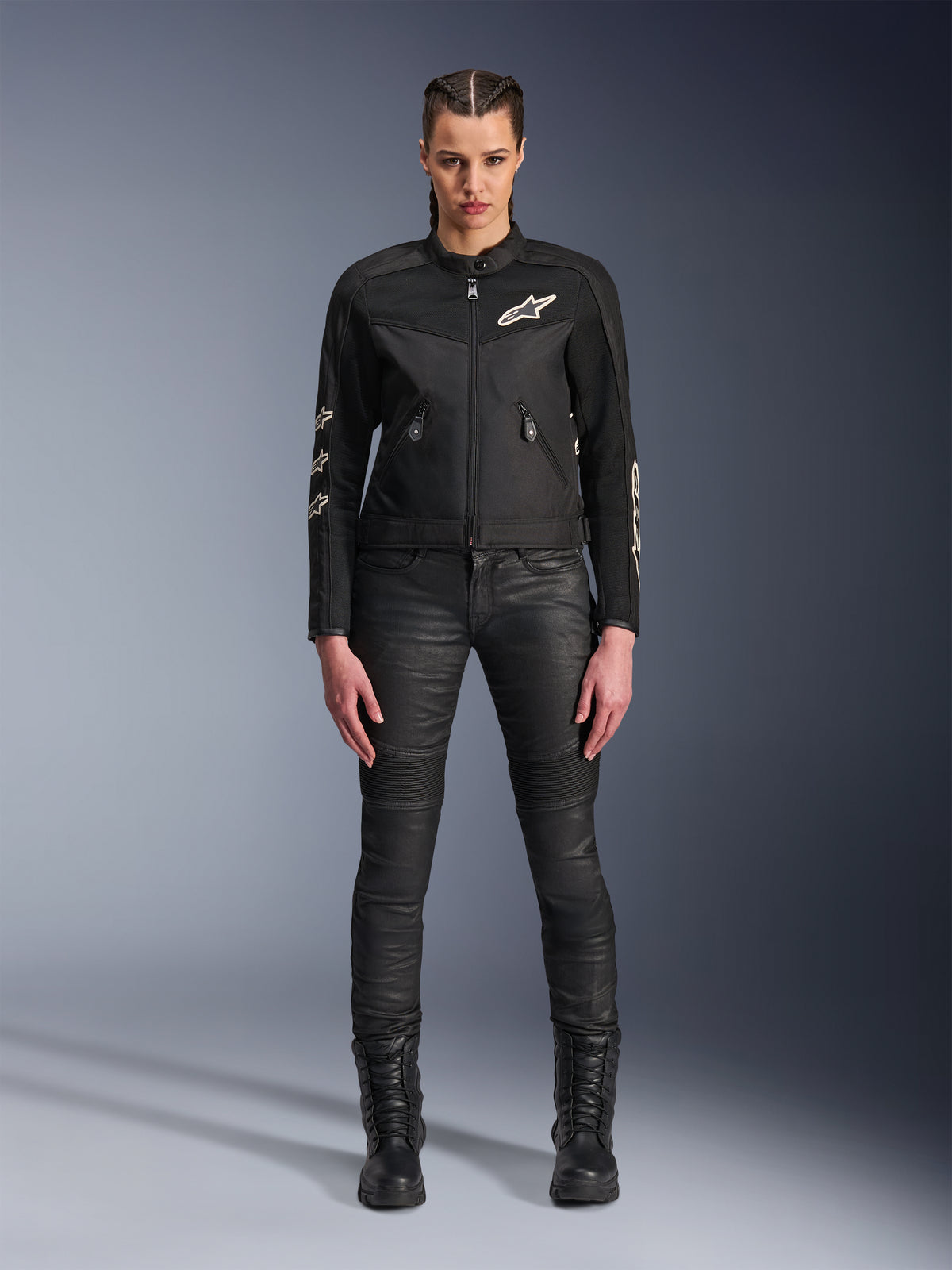 Female model wearing the Alpinestars Stella T-Dyno Air Jacket, Women's Motorcycle Jacket in Black, featuring 3D mesh panels and white Astars logos, paired with black slim-fit riding pants and black lace-up boots, urban riding gear style.