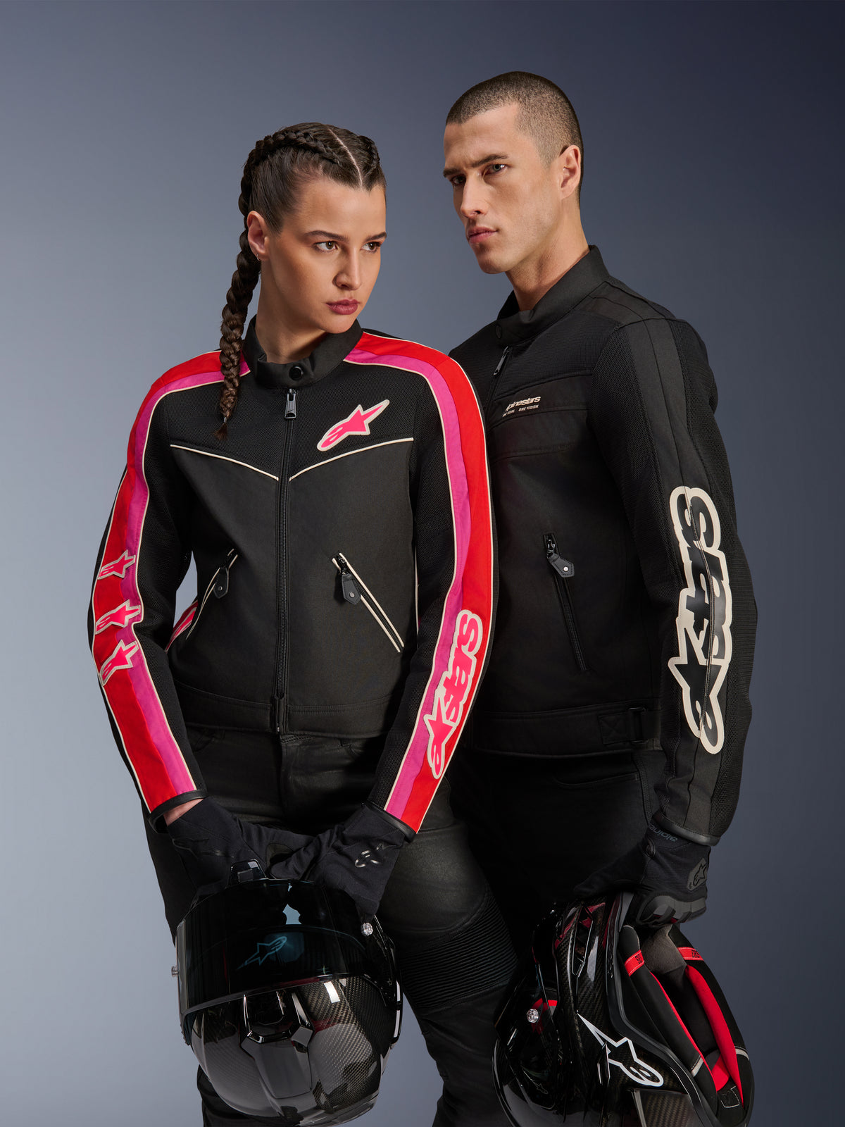 Alpinestars Stella T-Dyno Air-jacka på kvinna i Black Bright Red Fuchsia, matchad med svart Dyno Air-jacka för män, båda förarna håller motorcykelhjälmar, studiobild av urban modern motorcykelutrustning