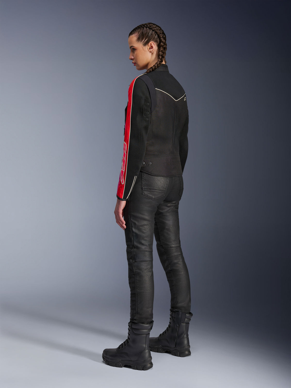 Kvinna iklädd Alpinestars Stella T-Dyno Air Jacket i Black Bright Red Fuchsia, matchad med svarta mc-byxor och svarta kängor, sidoprofil som framhäver den röda och fuchsiafärgade grafiken på ärmarna och den skräddarsydda biker-passformen.