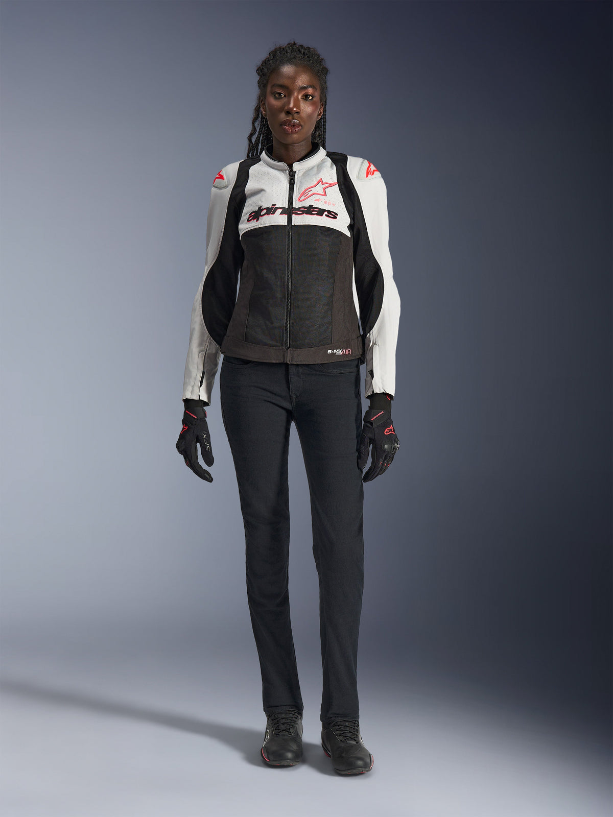 Alpinestars Stella SMX Air Jacket, Ice Gray Black och Coral Fluo, bärs av en kvinnlig modell med svarta mc-byxor och handskar, med nätchassi och skyddande axelsliders, sportmotorcykelutrustning för damer