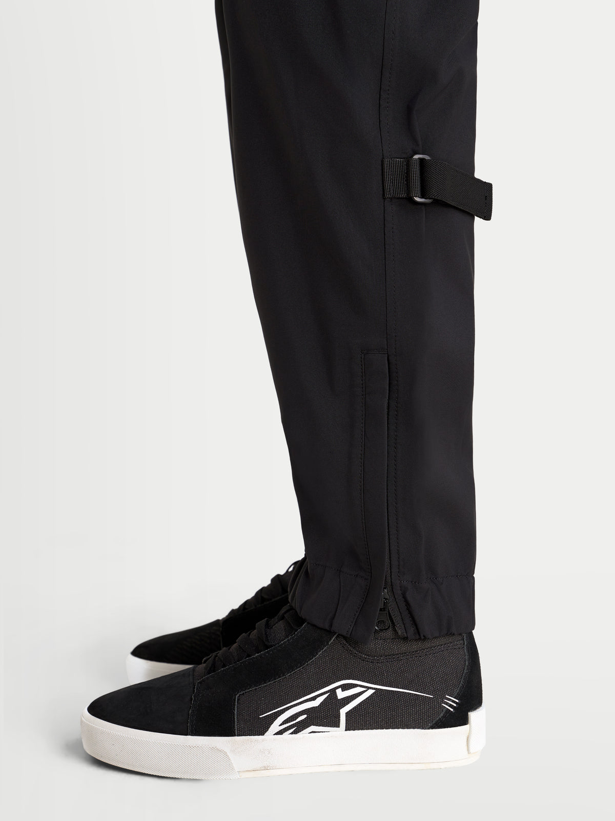 Alpinestars Juggernaut V2 Drystar byxor, svarta vattentäta motorcykelbyxor för stadskörning, nära bild från sidan som visar justering av benet och elastisk mudd med dragkedja, bärs av en modell