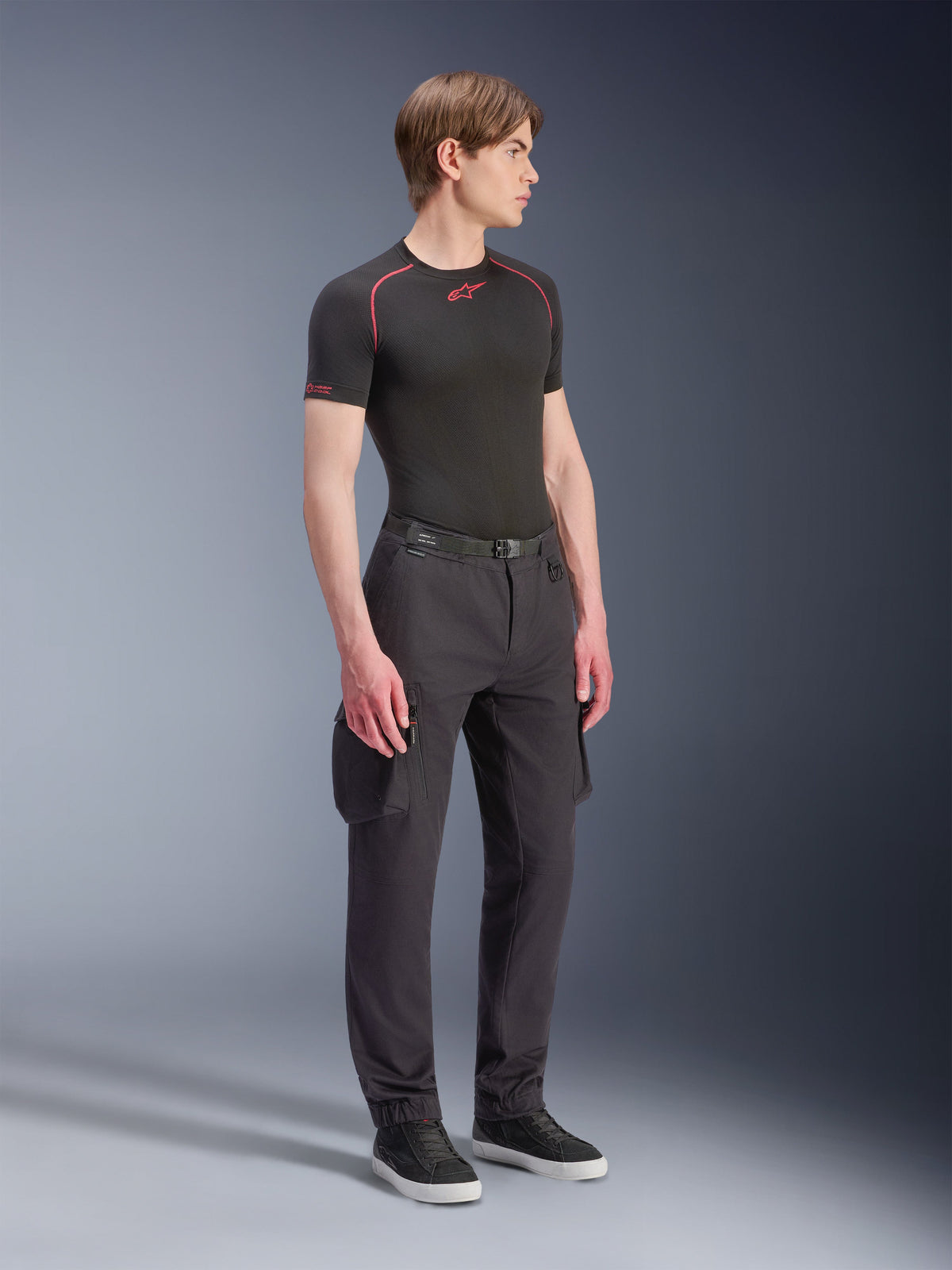Male model wearing Alpinestars Flex-AST Cargo Pants - Short in Black, urban motorcycle cargo pants with side pockets and tapered legs, styled with a black base layer and sneakers, urban riding apparel.