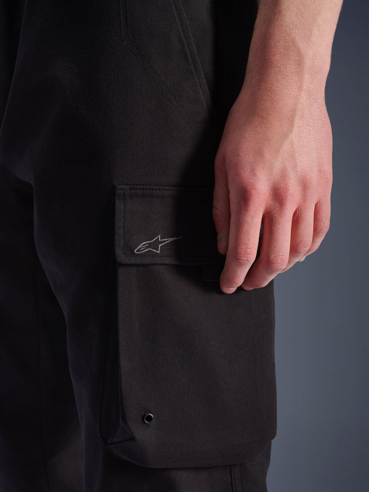 Alpinestars Flex-AST Cargo Pants, Urban Motorcycle Pants, Black, close-up of side cargo pocket with embroidered Astar logo, metal eyelet, and durable stretch twill texture