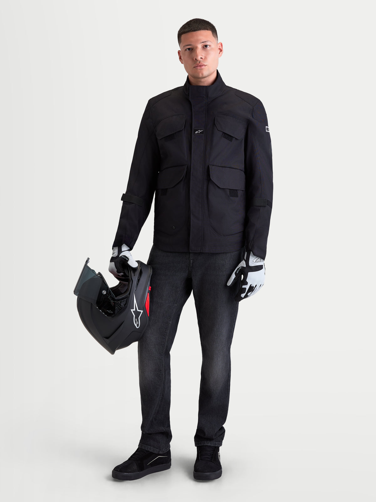 Alpinestars Flex Ast 8 Denim byxor, urban motorcykeljeans för herr i tvättad svart färg, bars av en manlig modell som håller i en hjälm och matchande utrustning