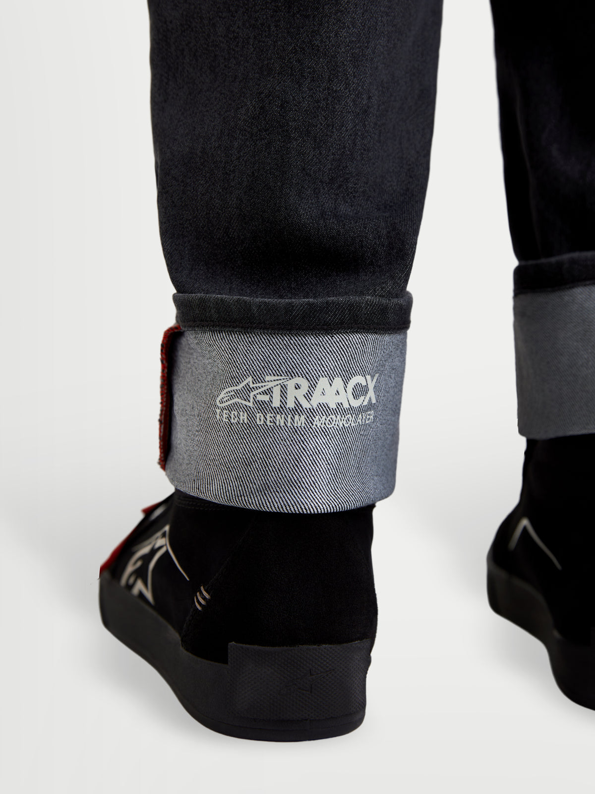 Alpinestars Flex Ast 7 Denim byxor, motorcykeljeans i urtvättad svart färg, närbild på uppvikta benslut med A-TRAACX teknisk denim-branding och stadkantdetalj