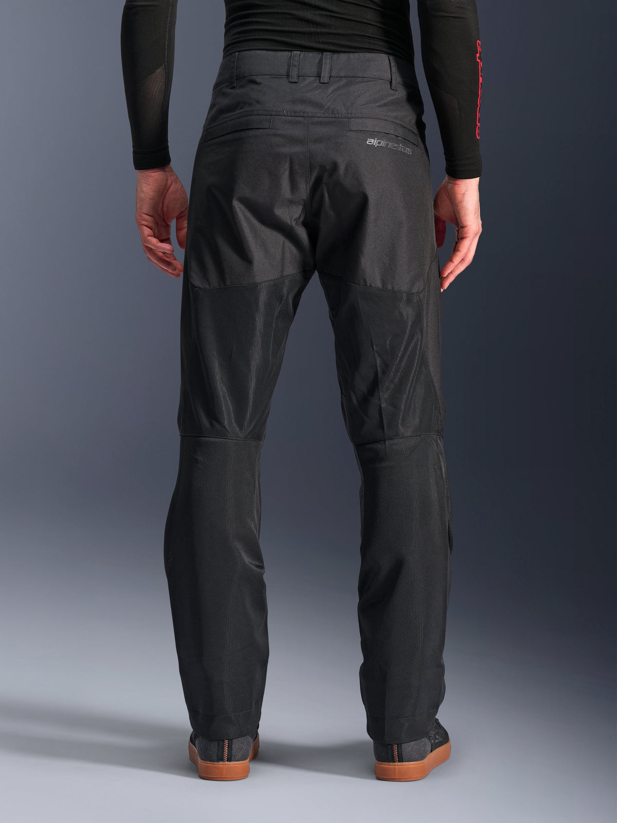 Alpinestars C-1 Air Byxor, vy bakifrån, svarta, urbana motorcykelbyxor i textil med stora paneler i teknisk mesh på baksidan av benen för ventilation, ren design med subtil logotyp, bärs med ett svart baslager och vardagliga körskor.
