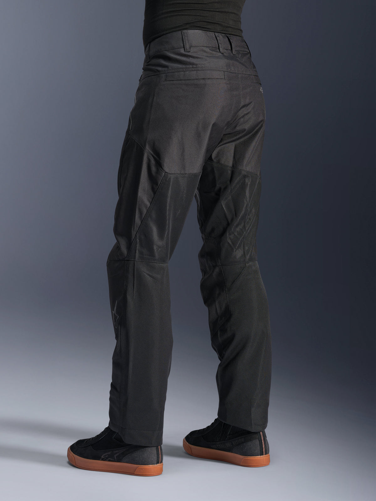 Alpinestars C-1 Air Byxor, urbana motorcykelbyxor, svarta, vy bakifrån som visar stora tekniska meshpaneler på baksidan av benen för ventilation, stilren design för stadskörning, bärs med avslappnade svarta sneakers