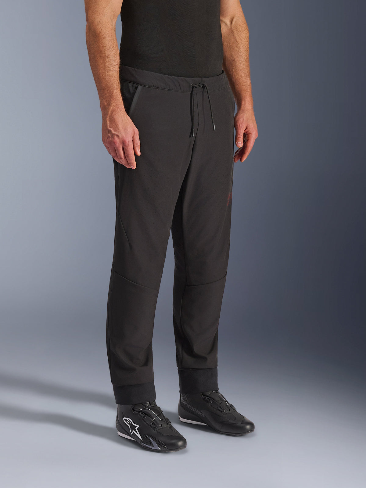 Alpinestars Aeroshell Airflow byxor, svarta motorcykelbyxor, bärs av modell med svarta körskor, med dragsko i midjan, ankelmuddar och laserperforerat softshell-tyg för maximal ventilation
