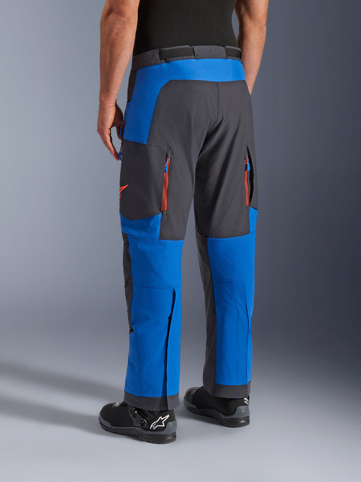 Alpinestars Maxdura Dual-byxor, kungsblå och mörkgrå, vy bakifrån som visar fickor med dragkedja och ventilationszoner, design för körning över stövlar bärs med svarta Alpinestars-stövlar, slitstark utrustning för äventyrs- och dual-sport-körning