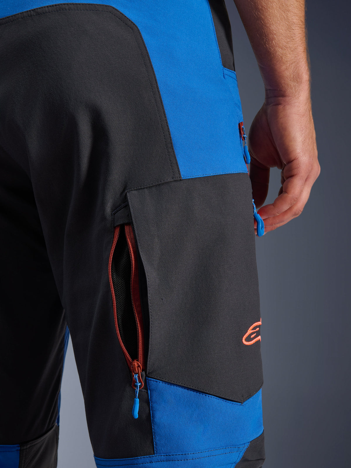 Alpinestars Maxdura Dual byxor, kungsblå och mörkgrå, närbild på cargoficka med dragkedja på sidan, blå dragtappar, orange broderad logotyp, motorcykelutrustning för äventyrskörning