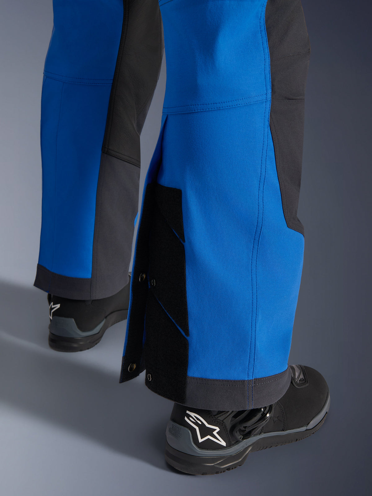 Alpinestars Maxdura Dual byxor, Royal Blue och Deep Gray, närbild på justerbart underben med tryckknappar och kil, design för äventyrskörning över stövlar, bärs med svarta Alpinestars motorcykelstövlar