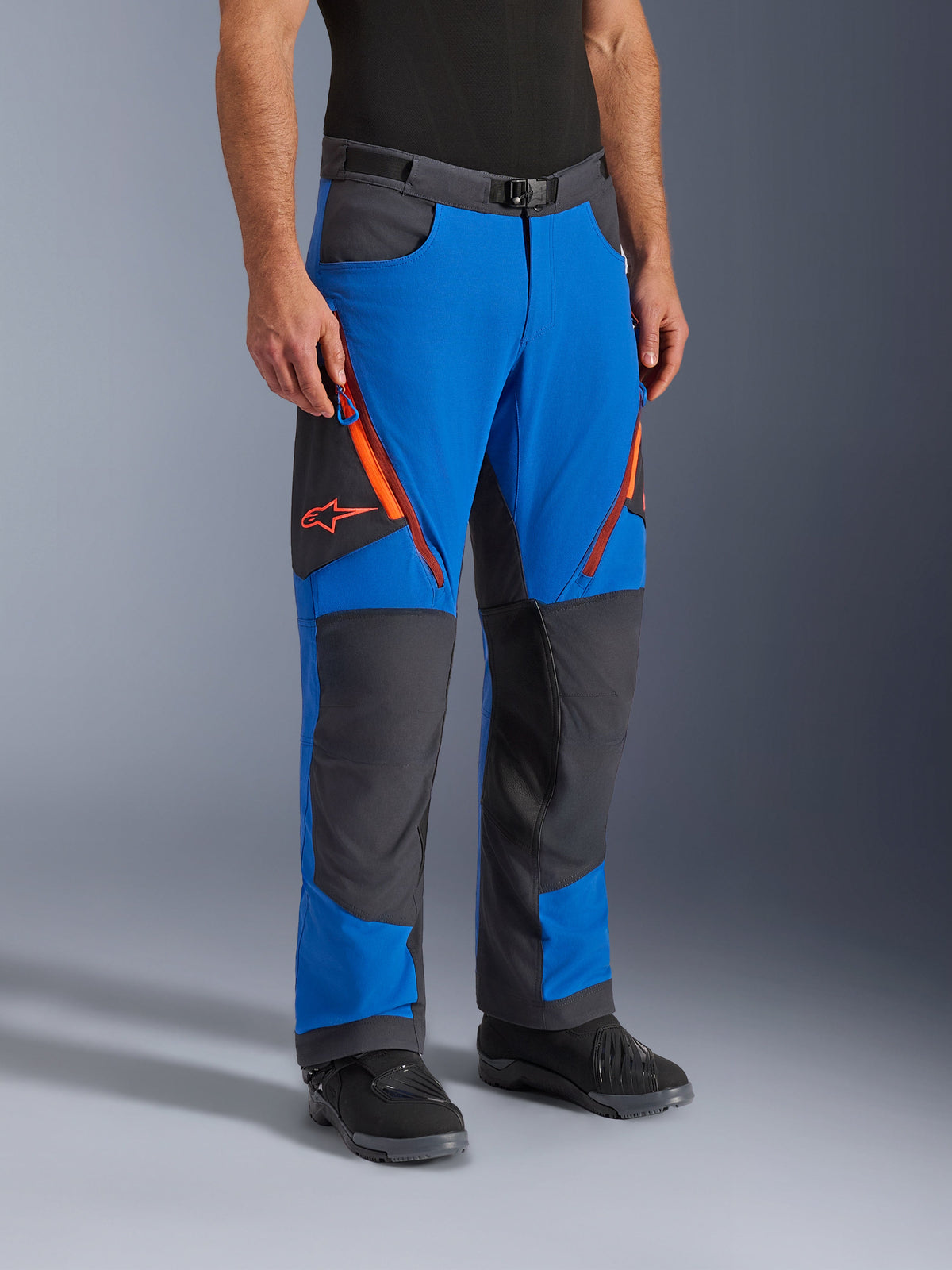 Alpinestars Maxdura Dual Pants, äventyrsmotorcykelbyxor, kungsblå och mörkgrå med orangea accenter, med ventilationsöppningar med dragkedja på låren, förstärkta knäpaneler och bälte med magnetspänne, teknisk över-stövel-design för dual-sport-körning.