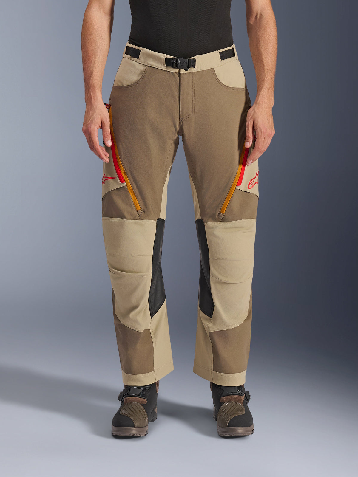 Alpinestars Maxdura Dual byxor, Walnut Aluminum, äventyrsmotorcykelbyxor med röda och orangea ventilationsöppningar med dragkedja på låren, svarta läderpaneler på knänas insida, bärs med ett svart underställ och robusta stövlar, hållbar design i flera färgtoner för dual-sport-körning