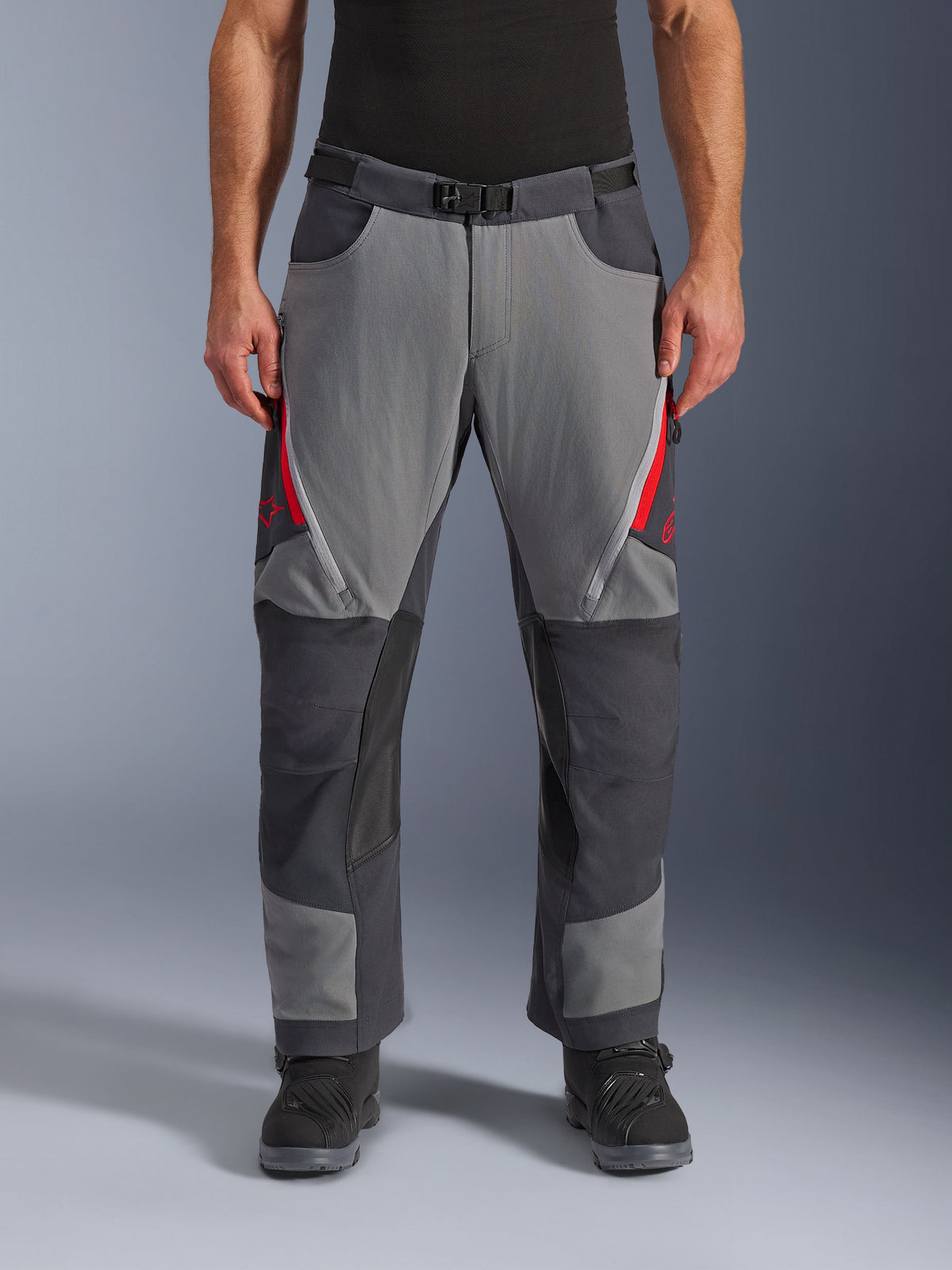 Alpinestars Maxdura Dual-byxor, adventure-motorcykelbyxor, mörkgrå och djupt grå med röda detaljer, vy framifrån som visar lårventilation med dragkedja, bälte med magnetspänne och förstärkta knäpaneler, design för att bäras över stövlar för dual-sport-körning