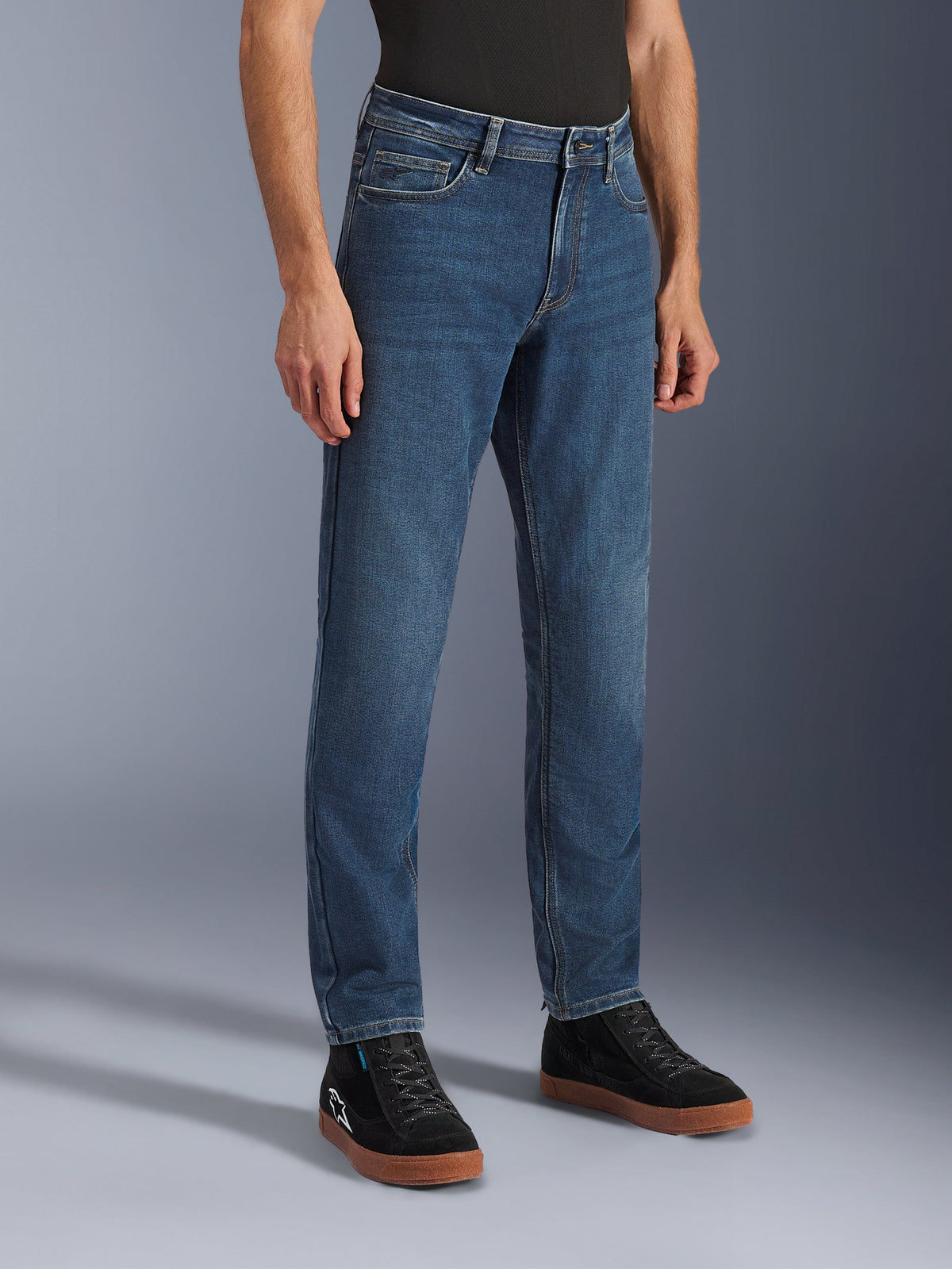 Alpinestars Flex-AST 5 Denim Pants, indigo-tvättade motorcykeljeans, regular tapered fit, bärs med svarta high-top sneakers och en svart tröja, avslappnad urban körutrustning med ett klassiskt denimutseende.