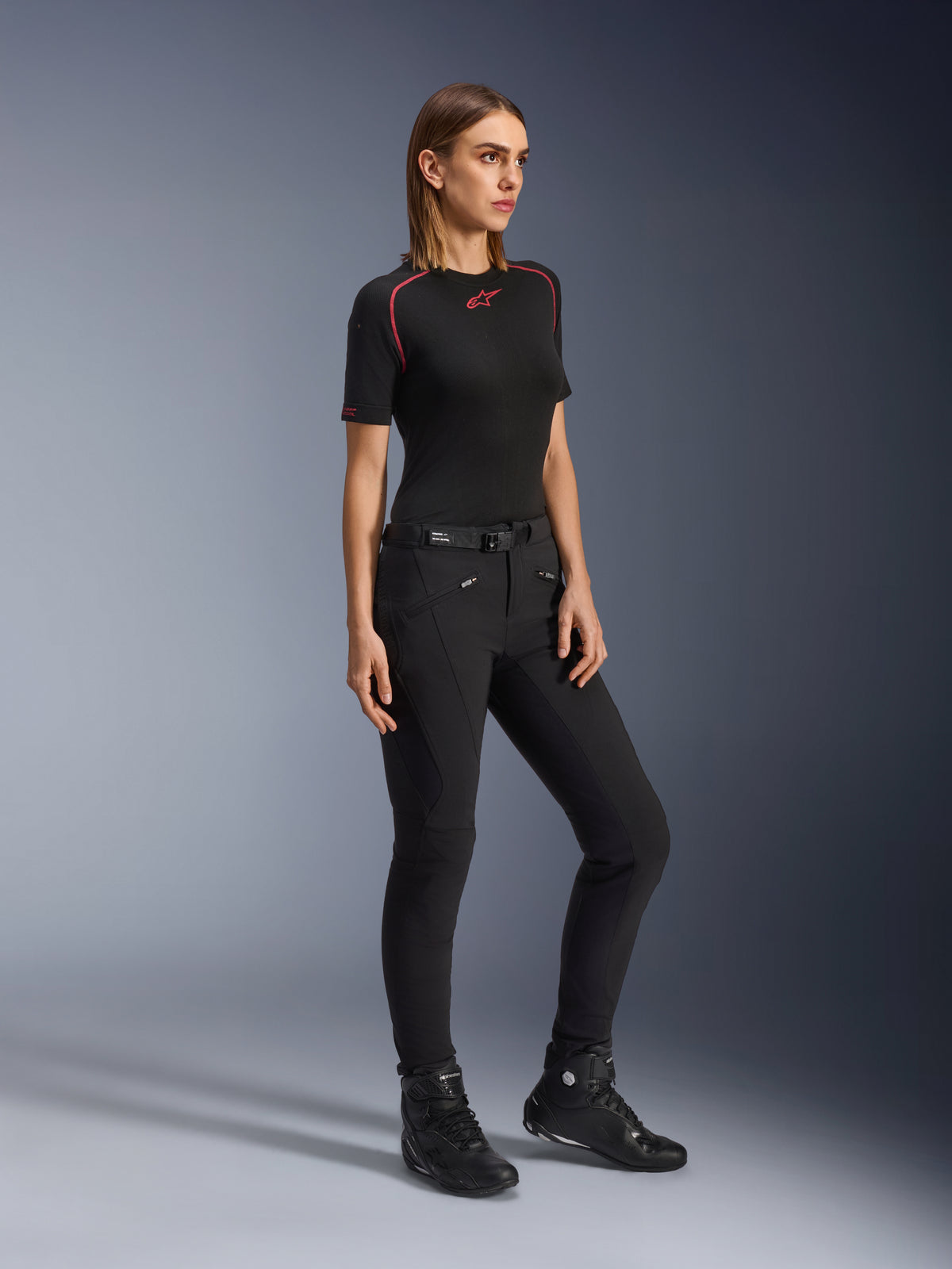 Alpinestars Alamosa Women Pants, svarta mc-byxor i slim-fit, bärs av en modell med svart underställ och körskor, har framfickor med dragkedja och ett midjebälte med magnetisk stängning, urban streetwear-stil.
